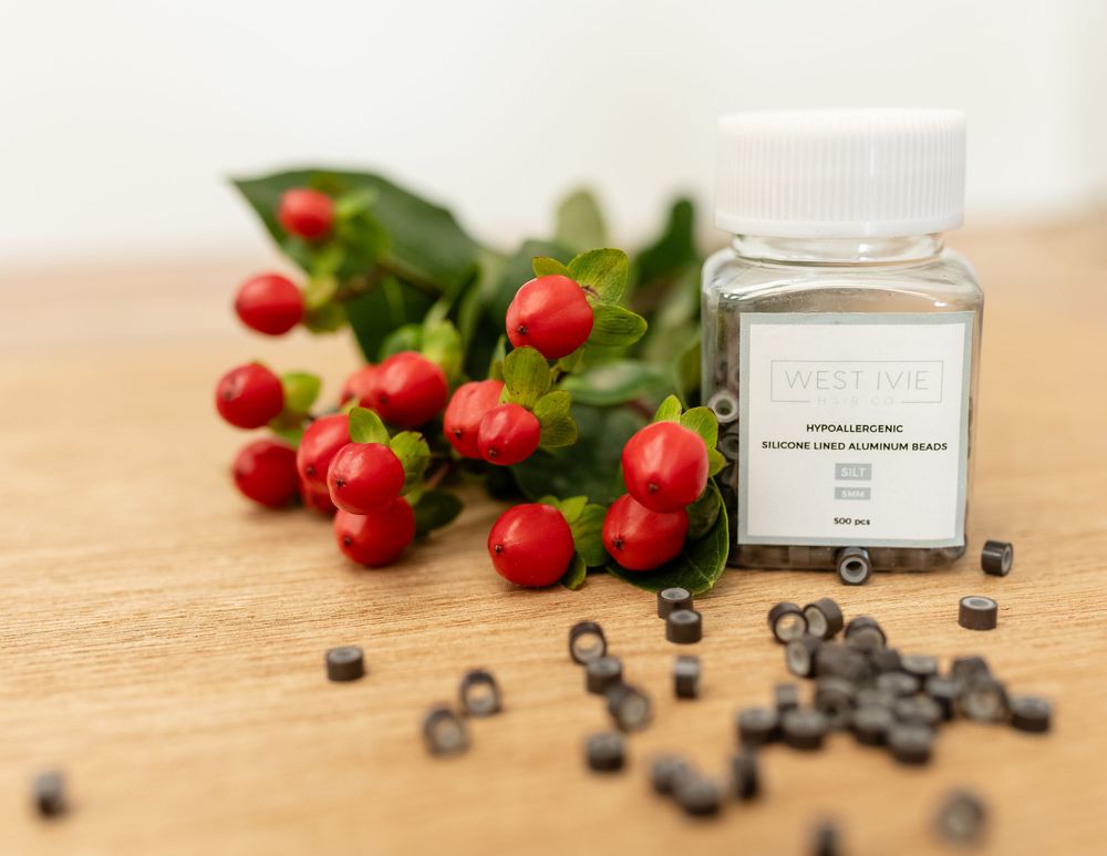 Glass jar of hair extension beads with red berries and foliage on wooden surface.