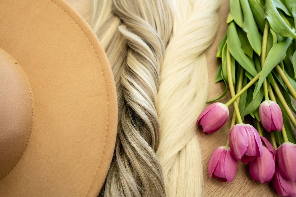 Tan felt hat with blonde hair extensions and pink tulips on wooden surface.