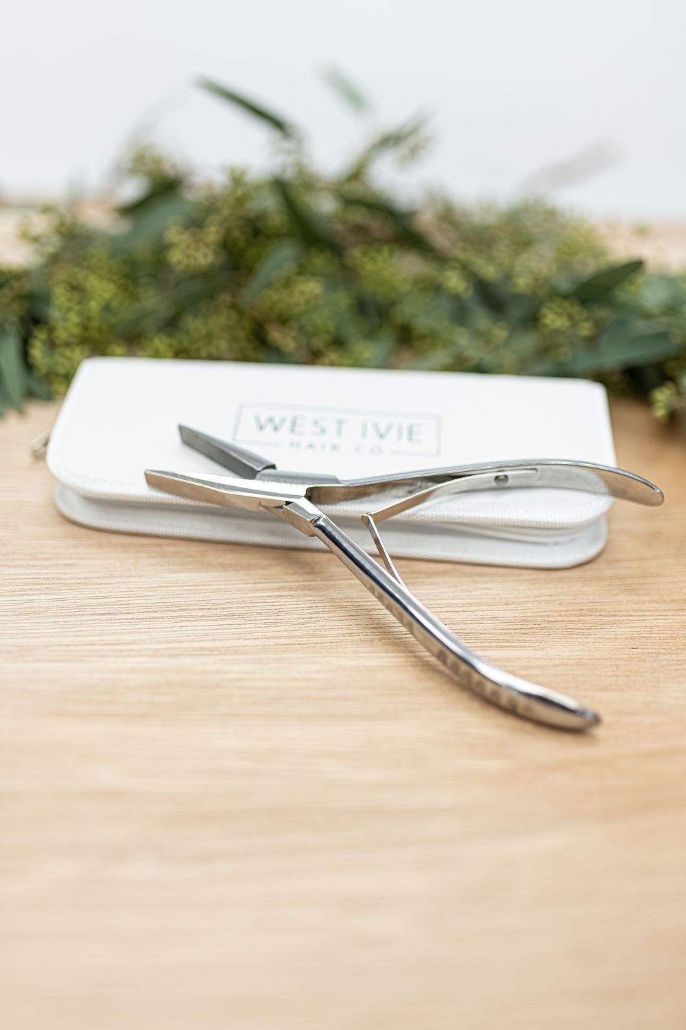 Professional hair cutting scissors with white case on wooden surface with greenery decoration.