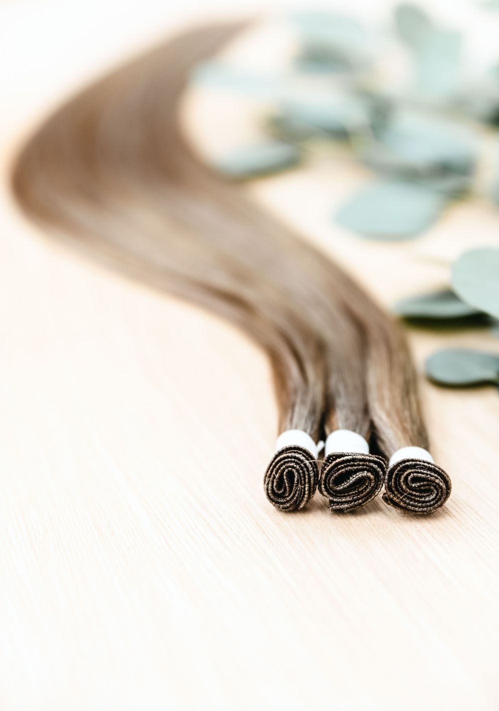 Close-up of brown hair extensions arranged artistically on light surface.