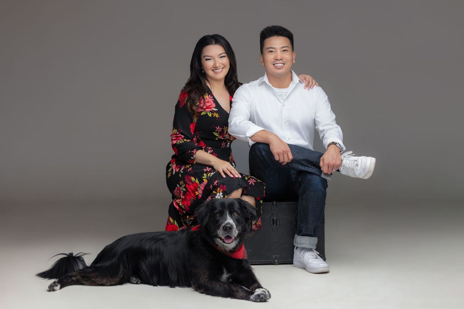 Professional intimate couple poses in dark moody studio with wooden chair against grey background for photography session.