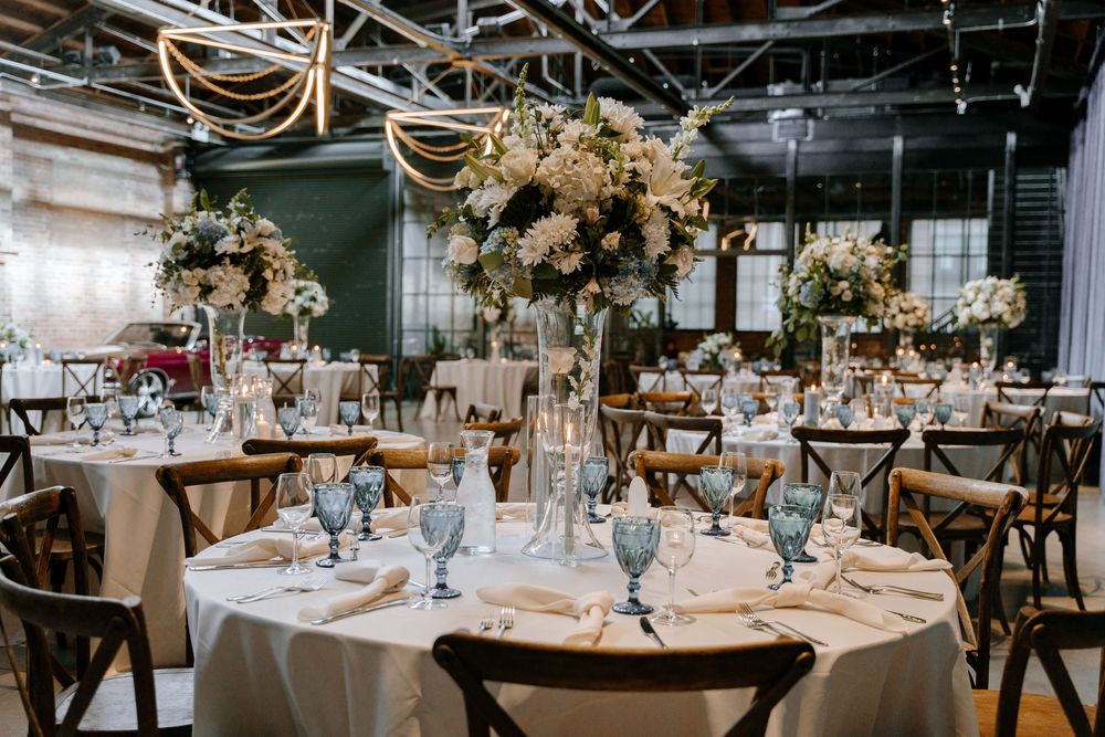 Elegant wedding reception tables adorned with lush floral centerpieces and crystal glassware in an industrial venue.