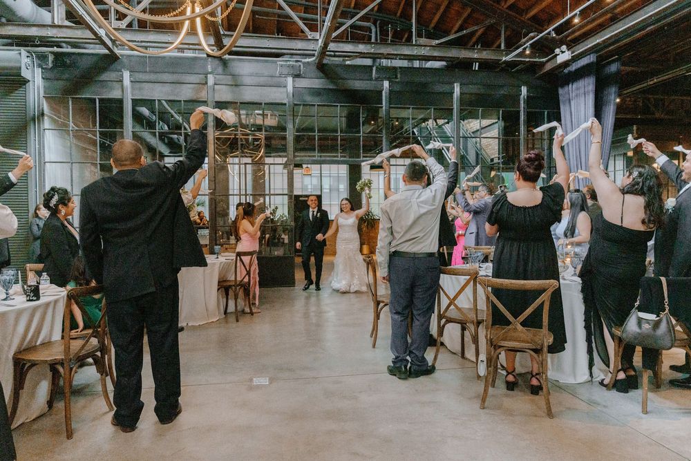 Wedding reception in a rustic industrial venue with exposed beams and string lights creating a warm ambiance.