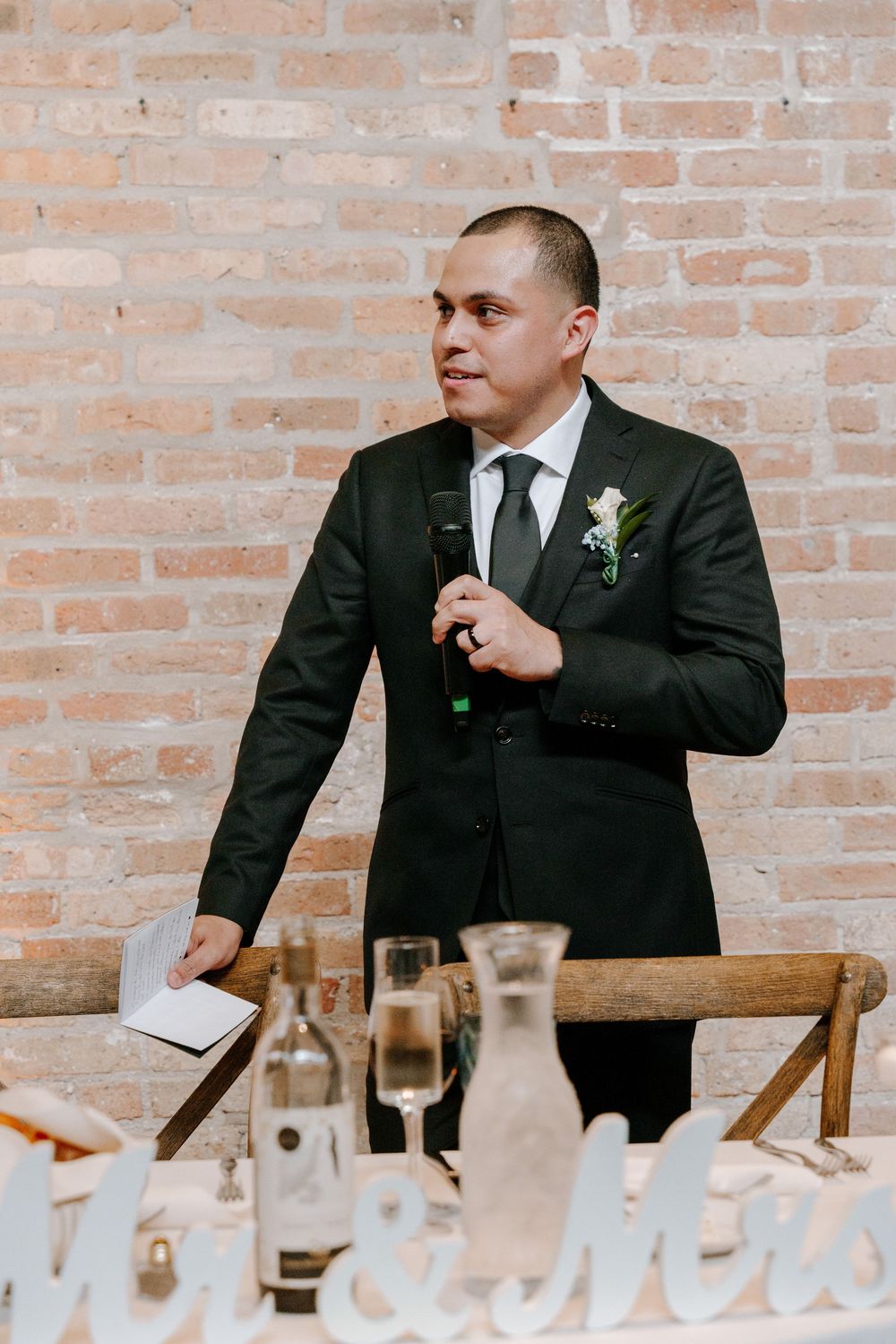 Split images show someone in a dark suit seated at a table with drinks and place settings against a brick wall.