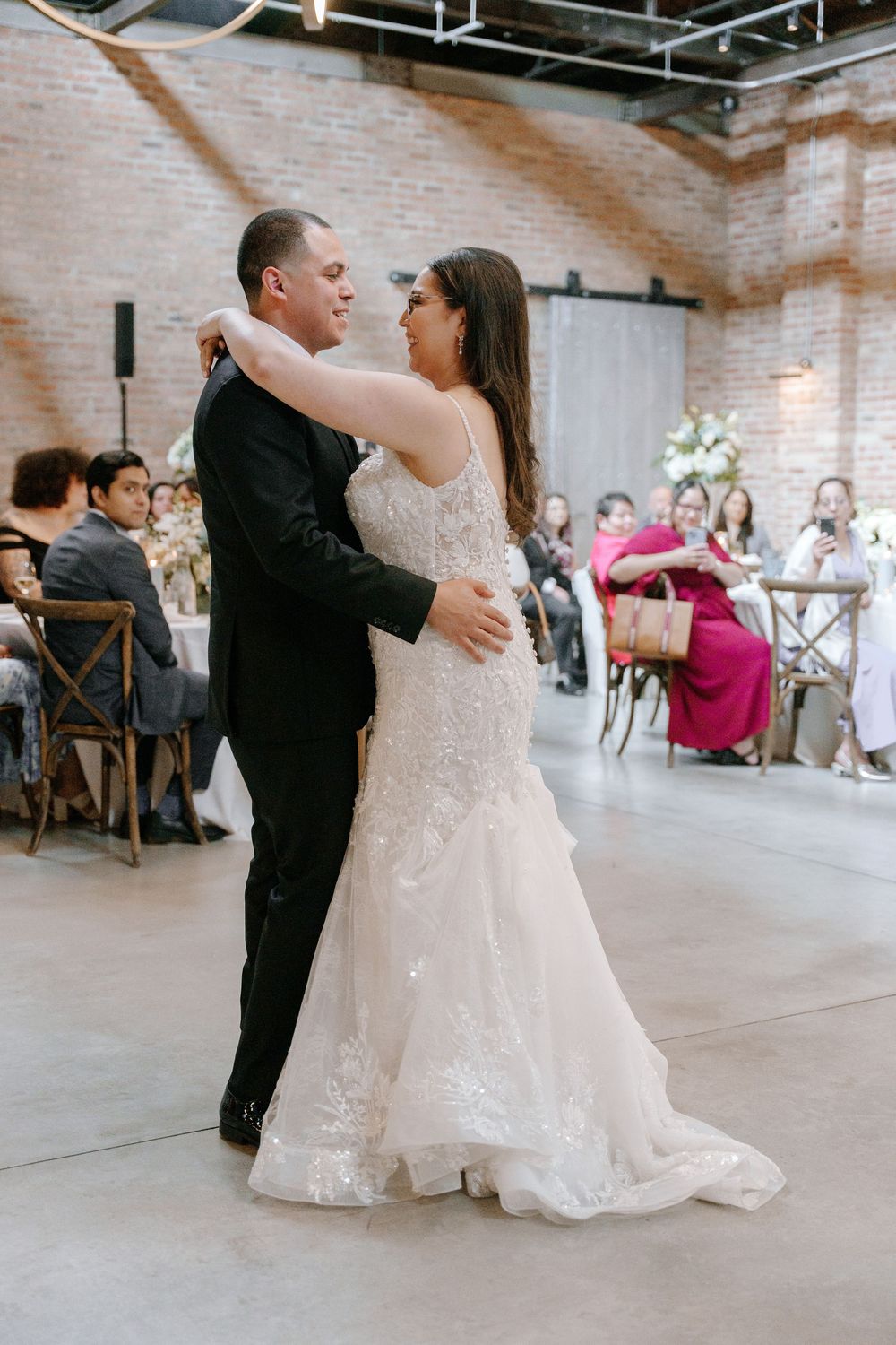 Wedding couple dancing together in a rustic industrial venue with exposed brick walls.