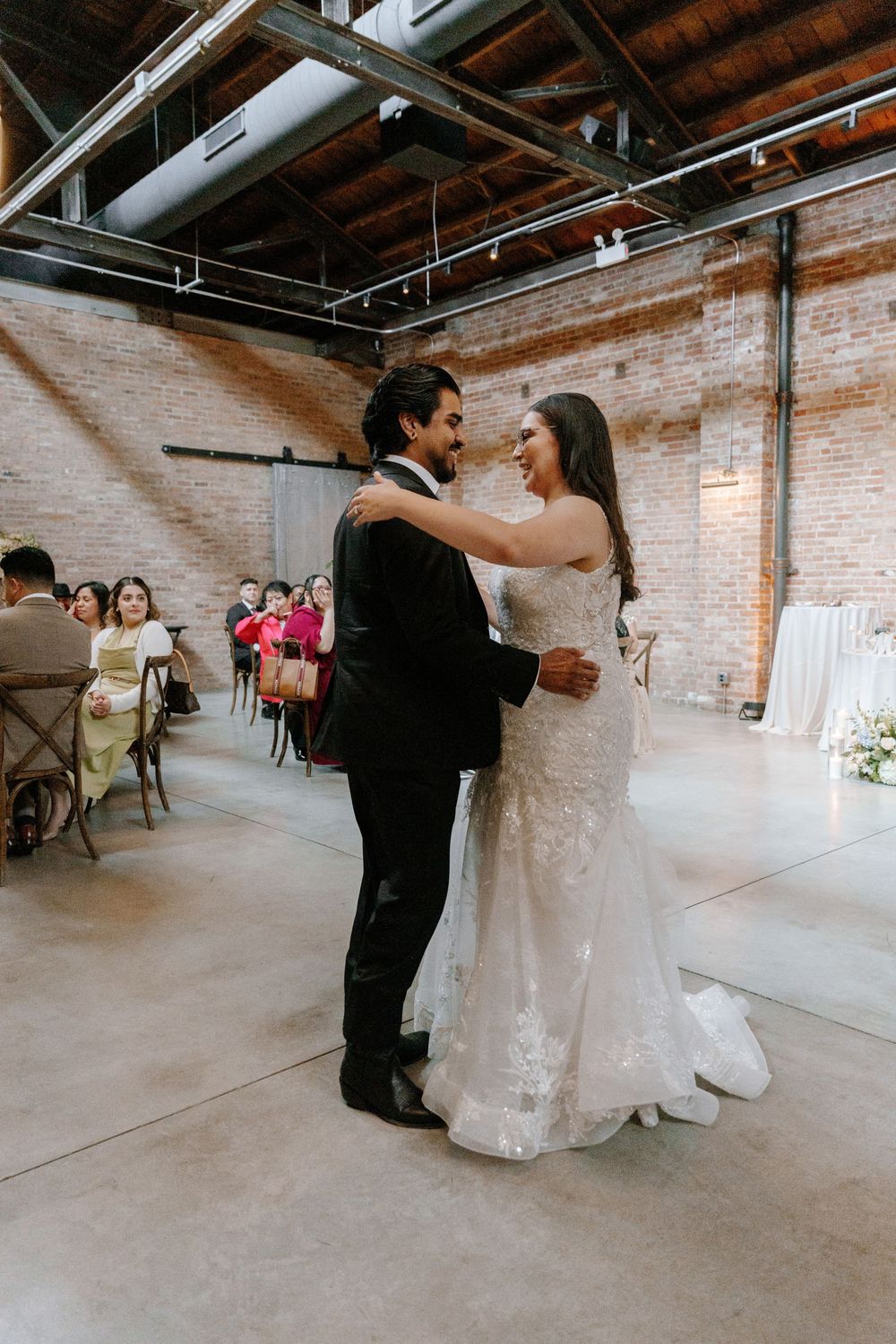 Wedding couple dancing together in an industrial venue with exposed brick walls and wooden beams.