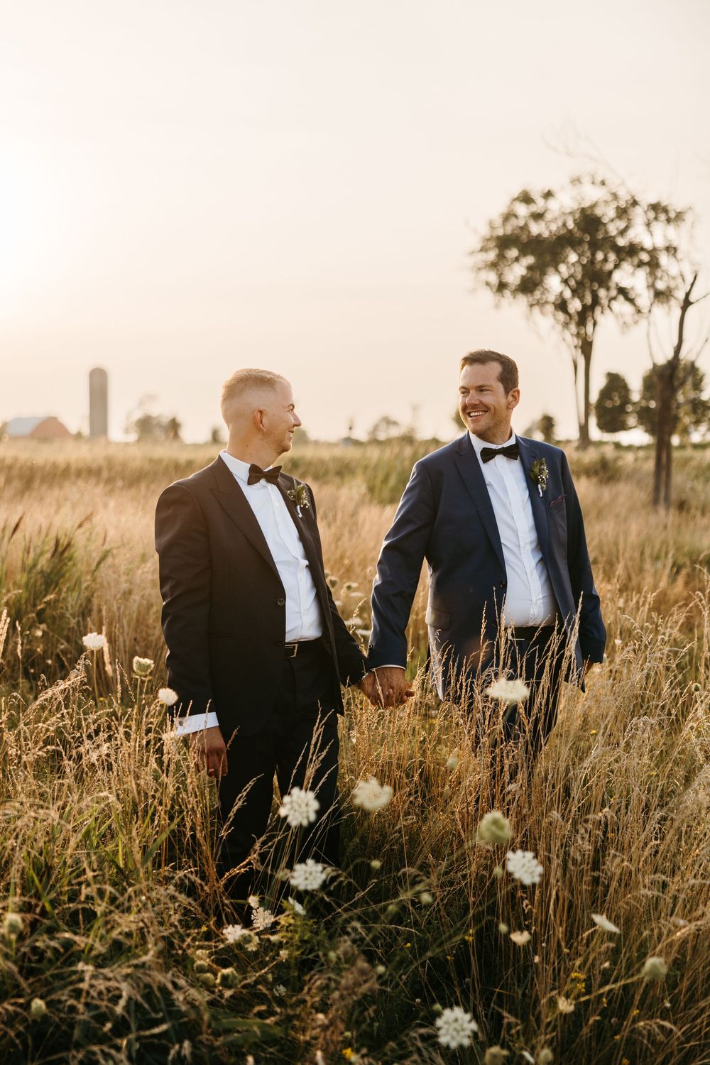 A group of people in formal attire stand together in a golden field at sunset, creating a silhouetted effect.