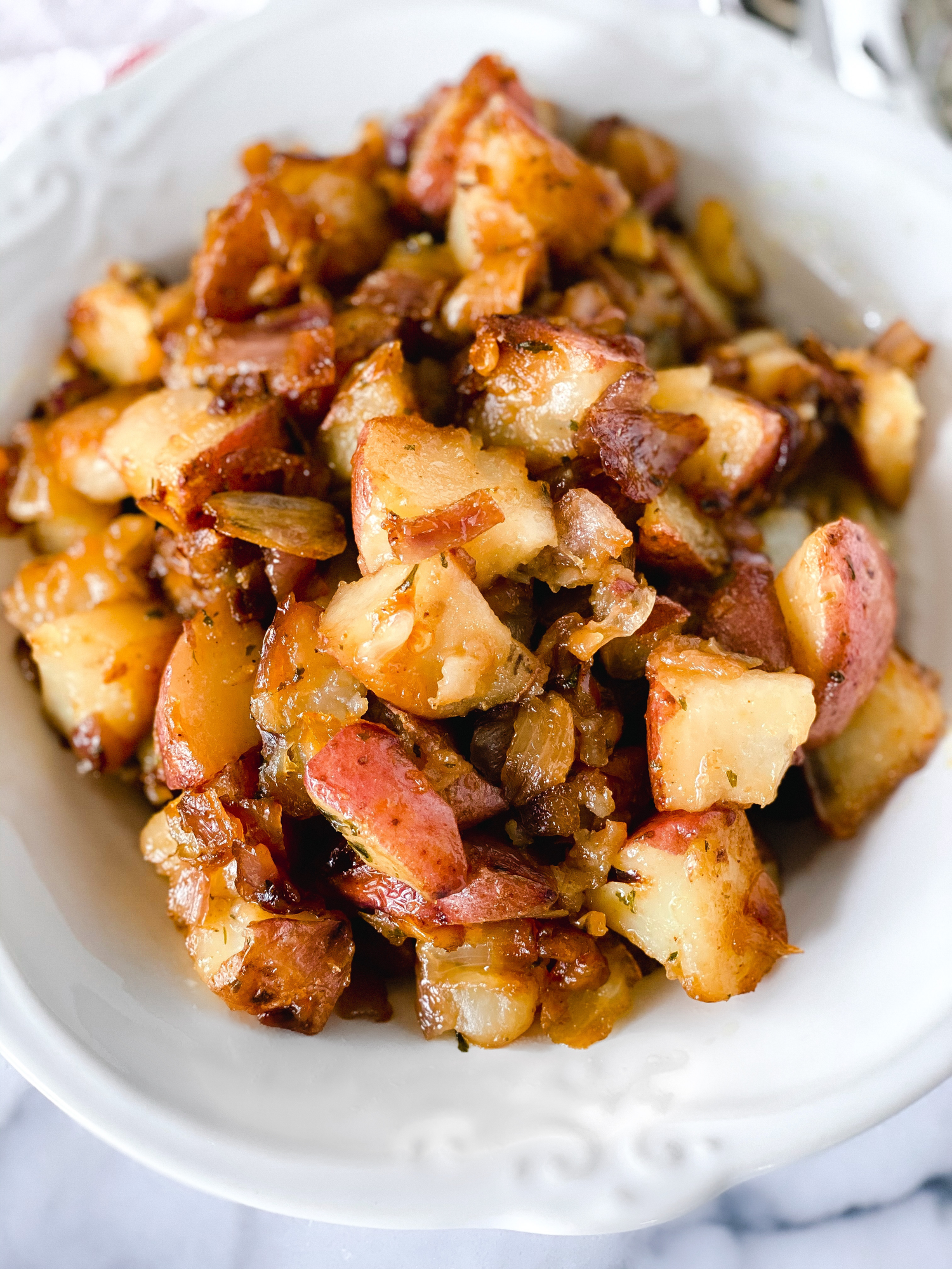 Crispy roasted potatoes with caramelized onions and herbs in a white bowl.