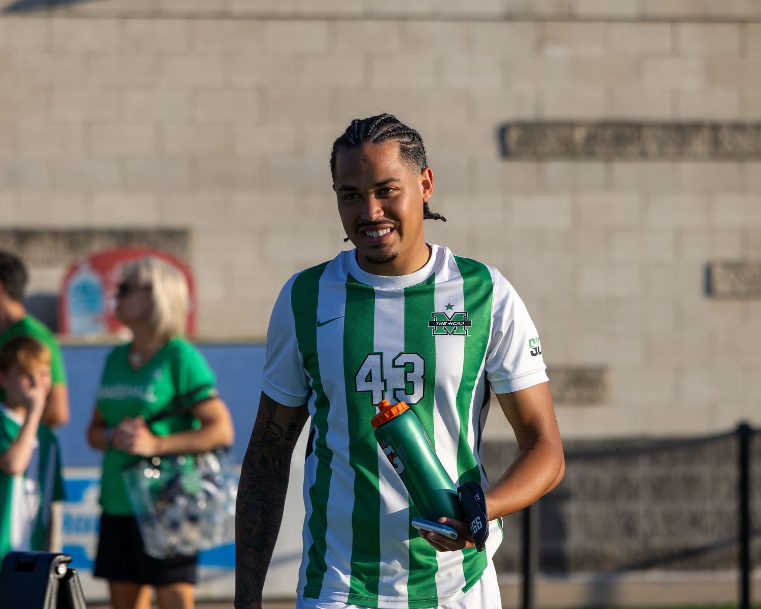 Soccer player in green and white striped jersey with number 45 smiles during outdoor match.