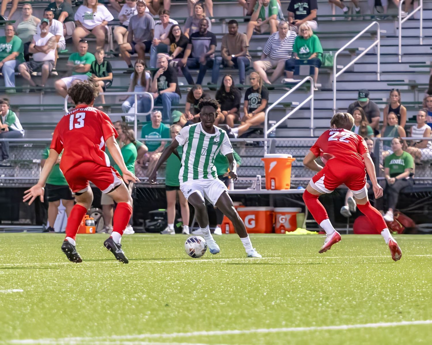 Soccer players in red and green striped jerseys compete for possession of the ball during an outdoor match.