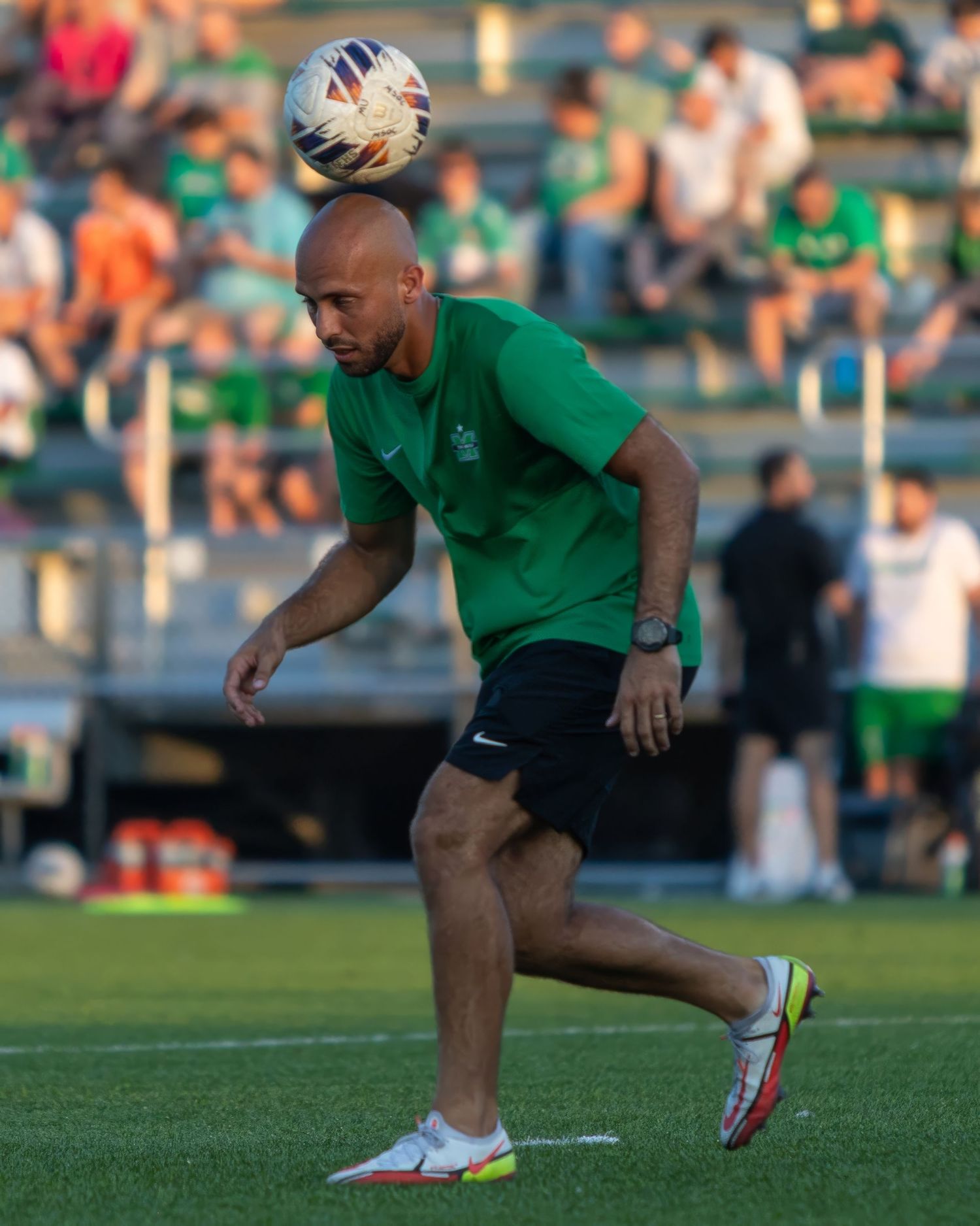Player in green jersey practices soccer ball control during outdoor training session.