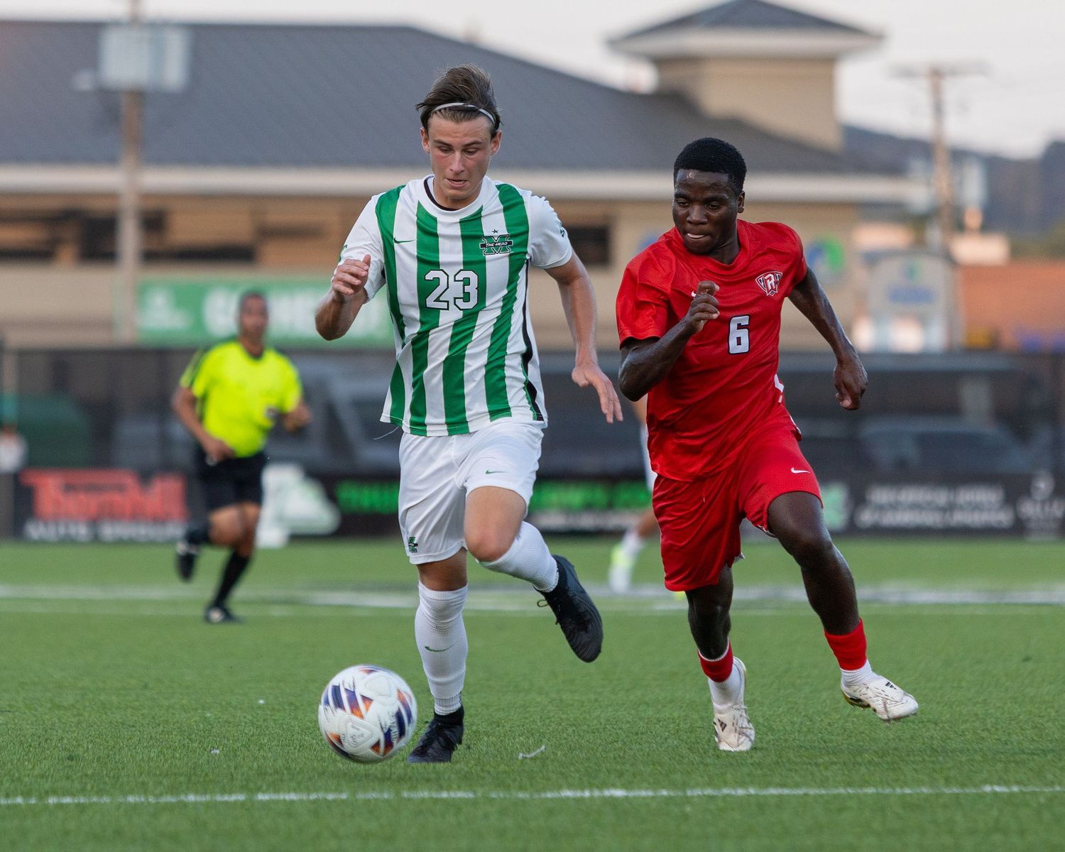 Two soccer players battle for the ball during a match with one in green and white stripes and another in red uniform.