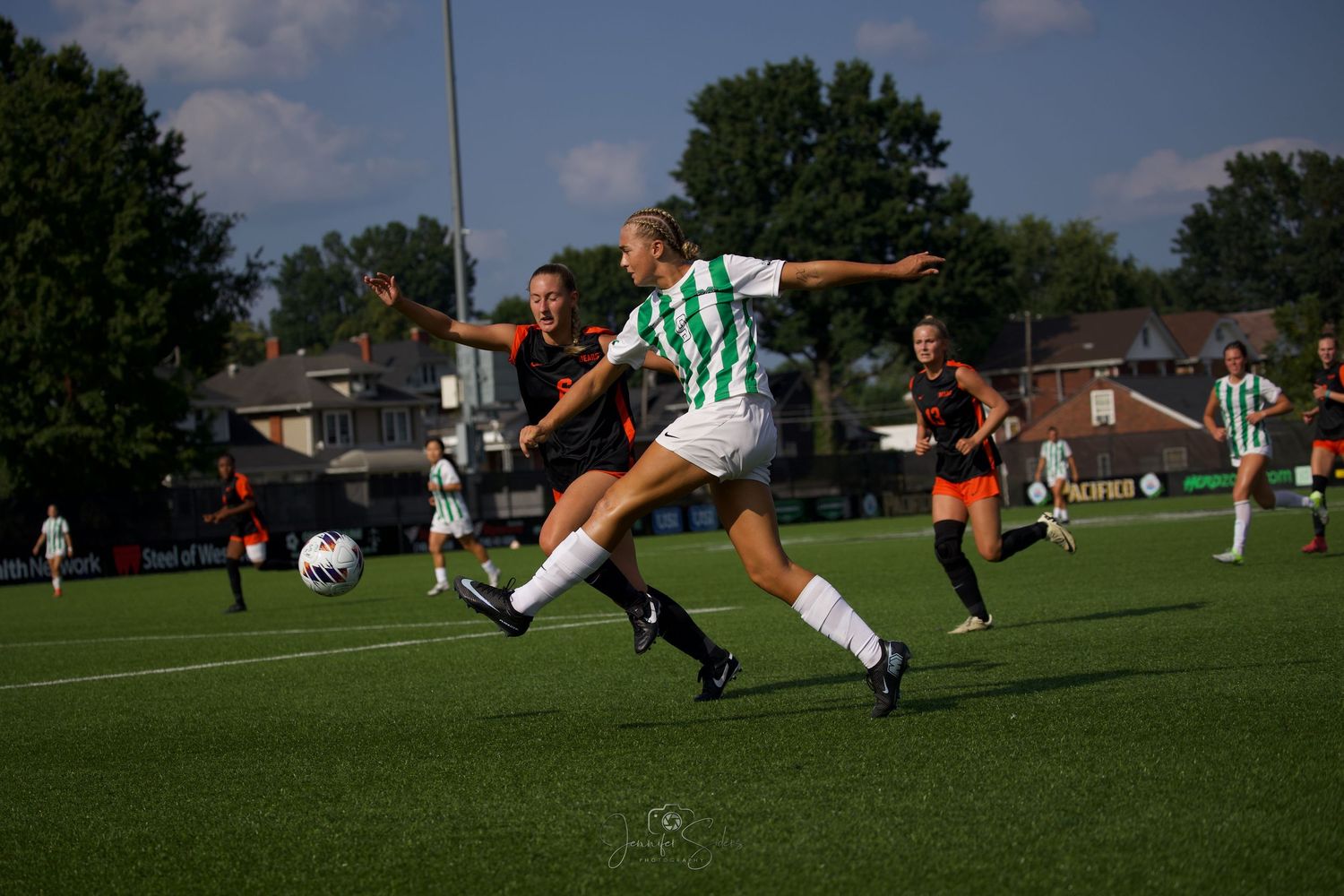Two soccer players battle for possession of the ball on a sunny grass field during a competitive match.