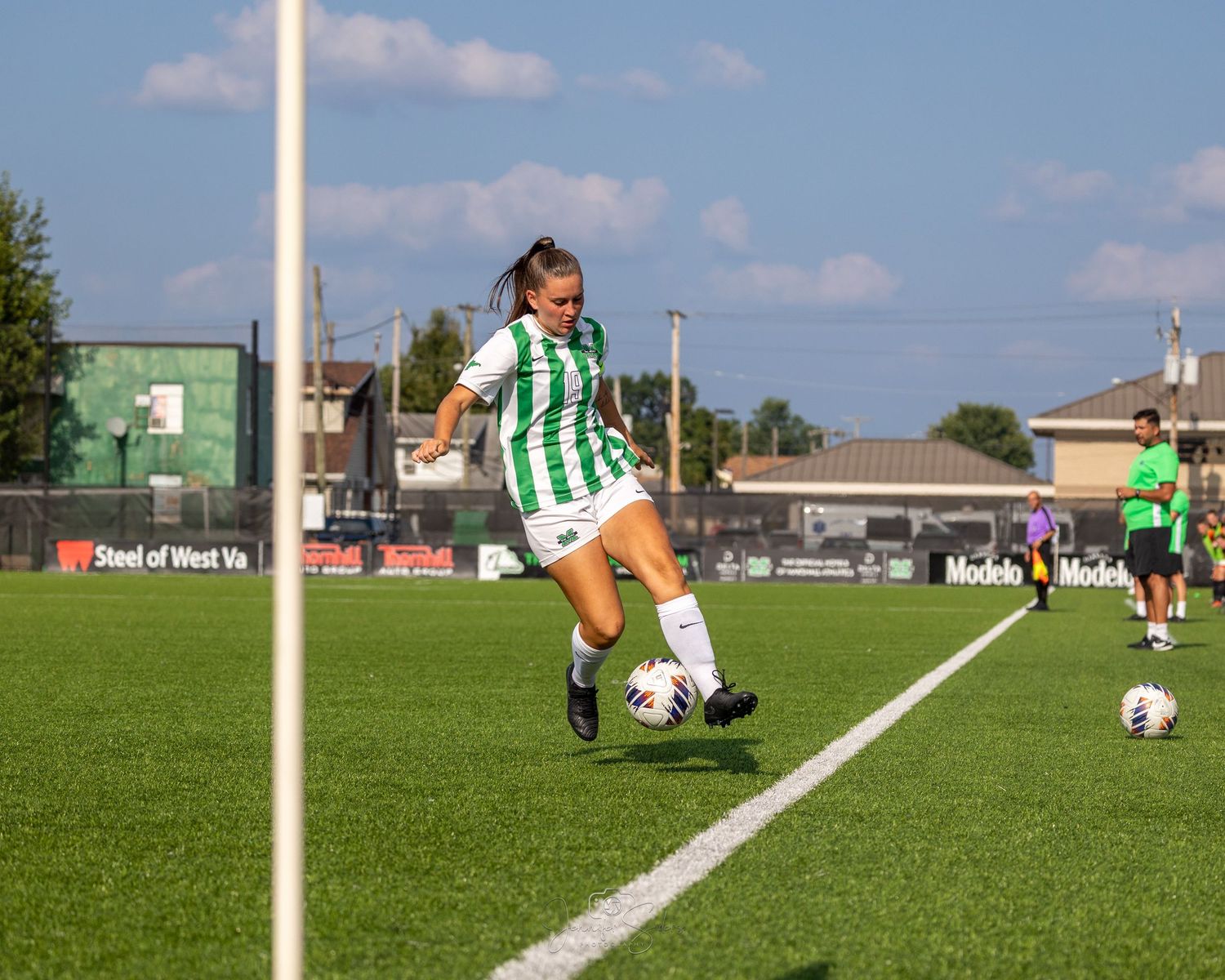 Female soccer player makes a precise kick on a sunny green field during a competitive match.