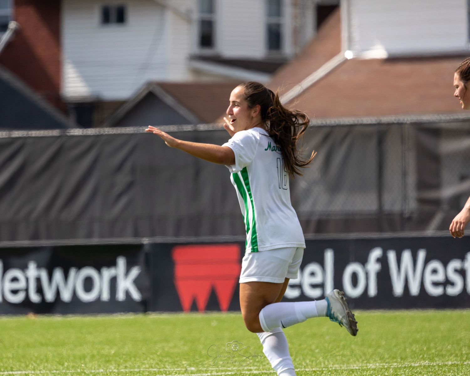 Women's soccer match in progress as players compete on field with stadium backdrop and advertising boards visible.