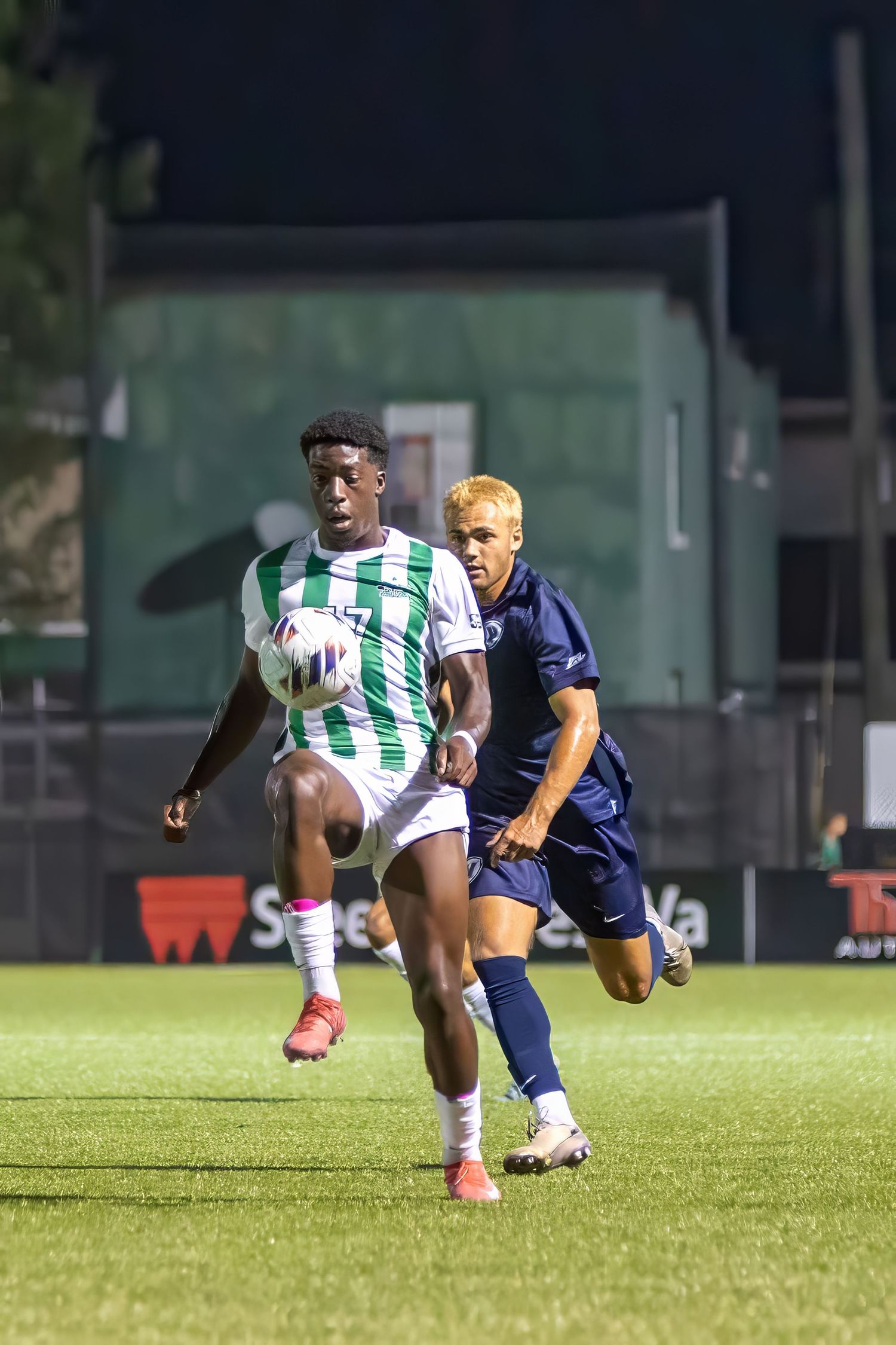 Soccer players compete for the ball during an intense match on a well-maintained grass field at night.