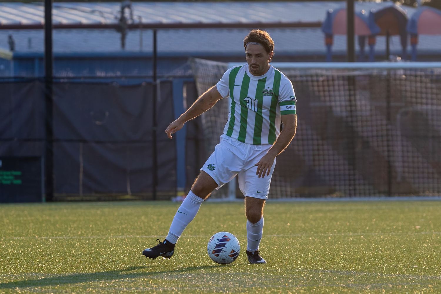 Soccer player in striped green and white jersey controls the ball on an outdoor turf field during a match.