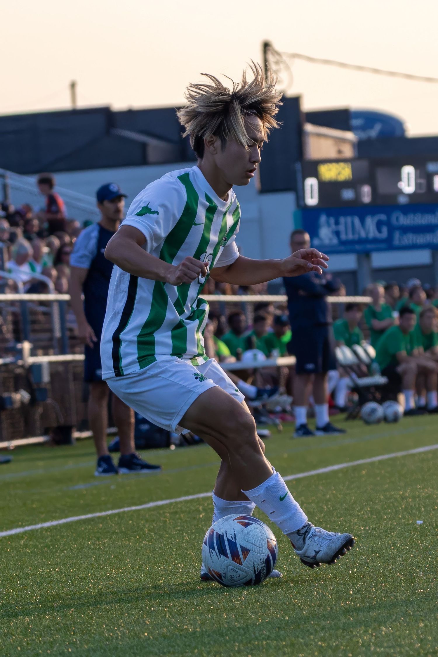 Soccer player wearing white and green striped uniform performs sliding kick on turf field during match.