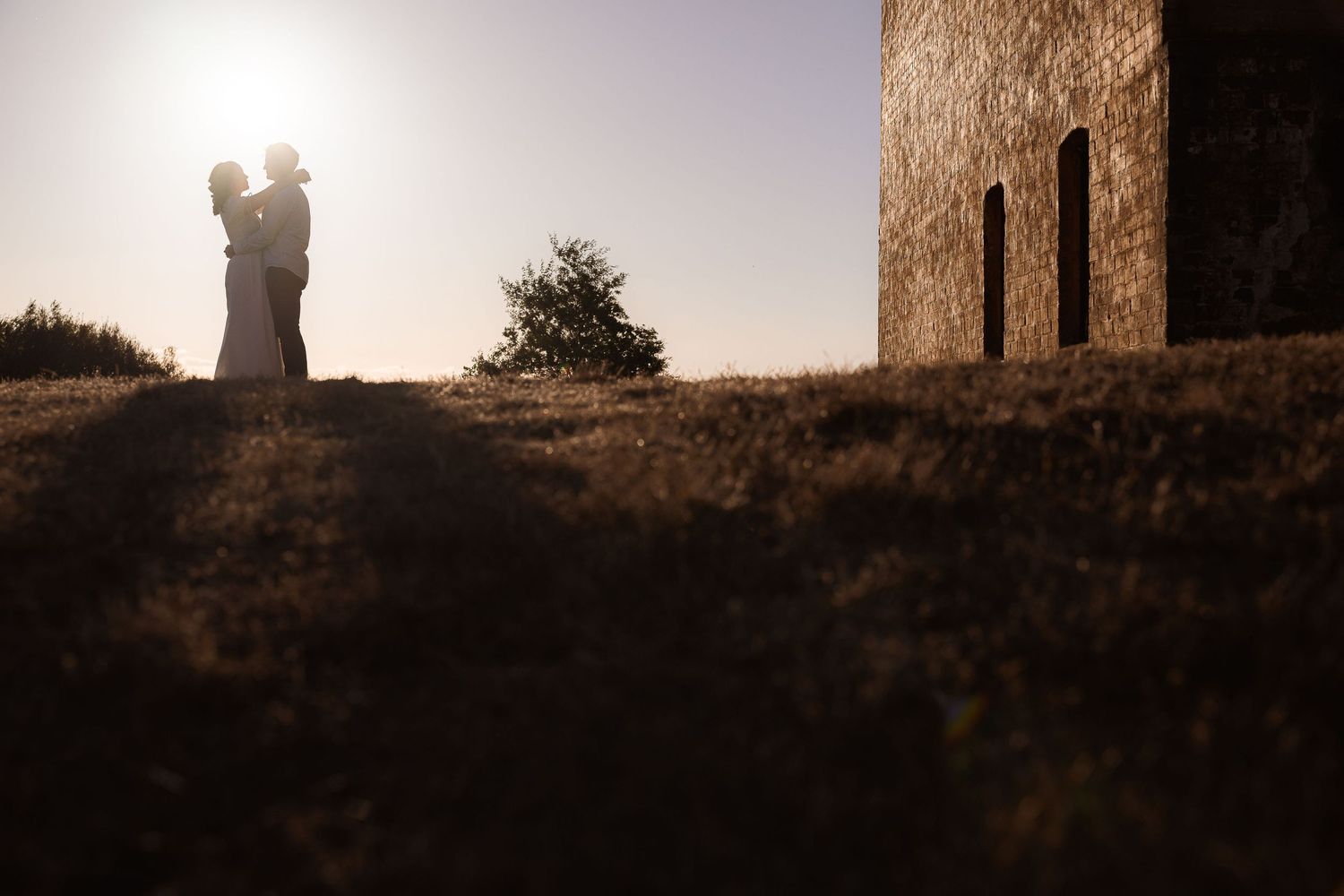 A silhouette stands against a golden sunset beside a stone tower in a tranquil landscape.