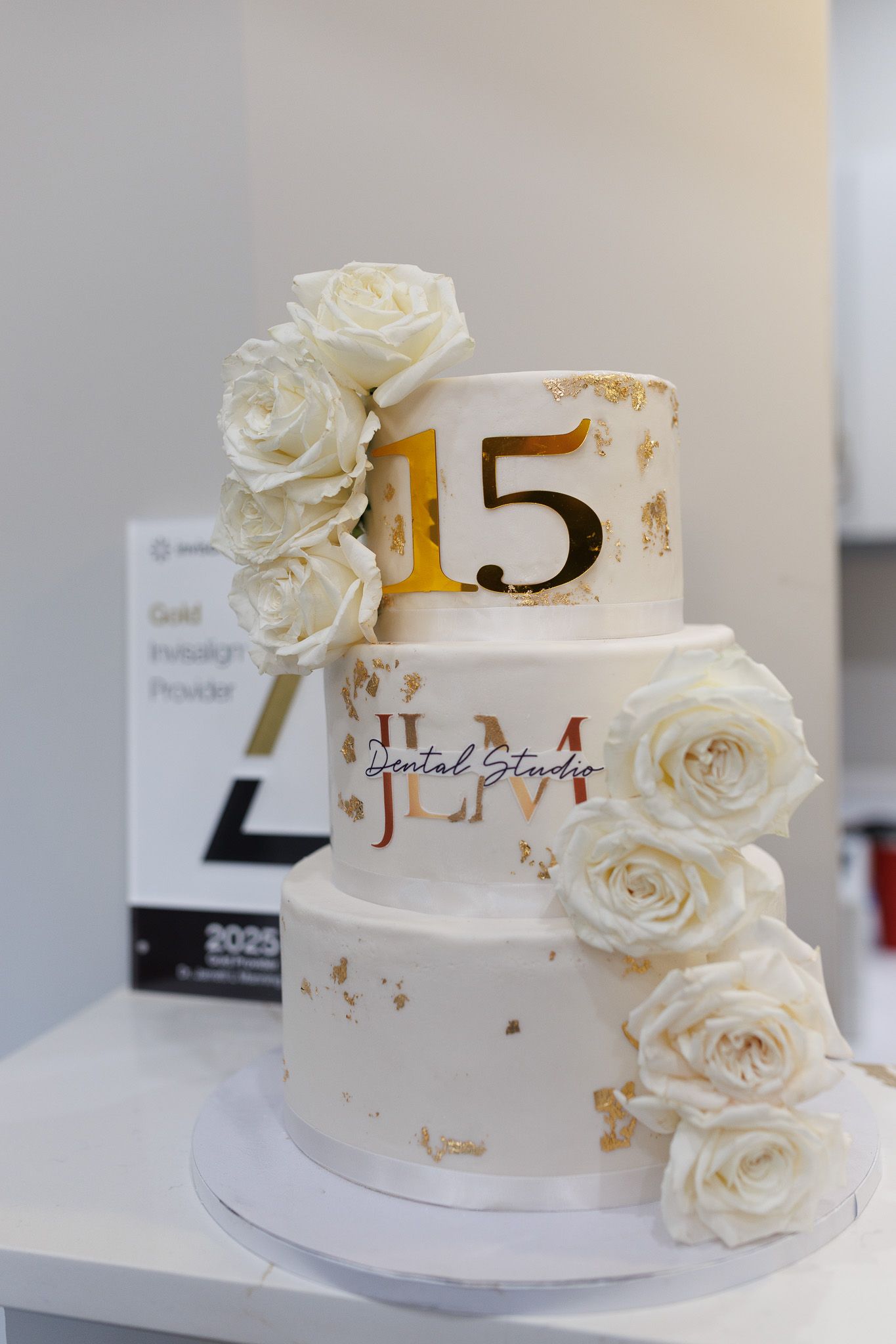 Elegant white tiered cake decorated with gold accents and cascading white roses for a 15th anniversary celebration.