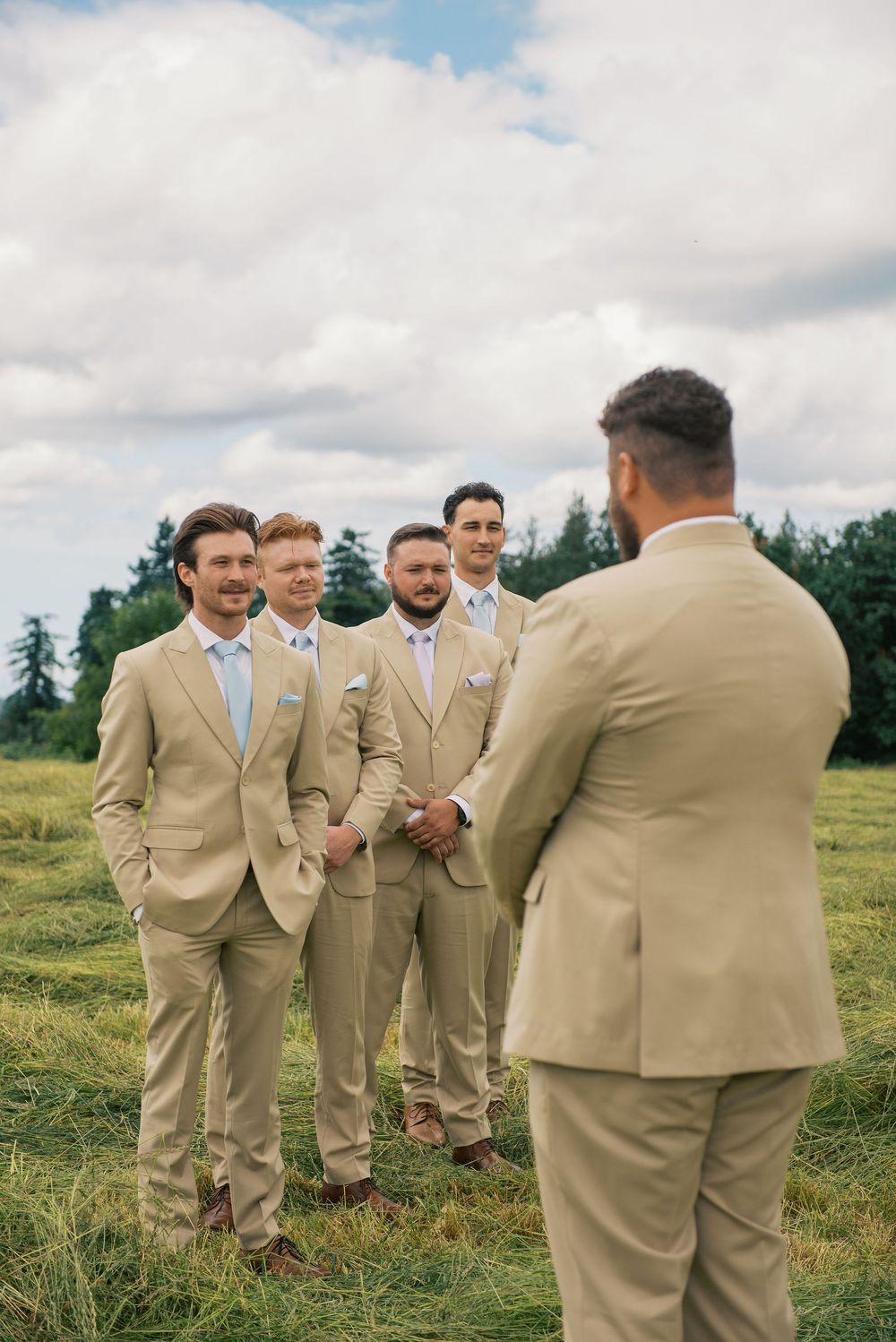 Groomsmen in khaki suits gather on a hillside for wedding photos.