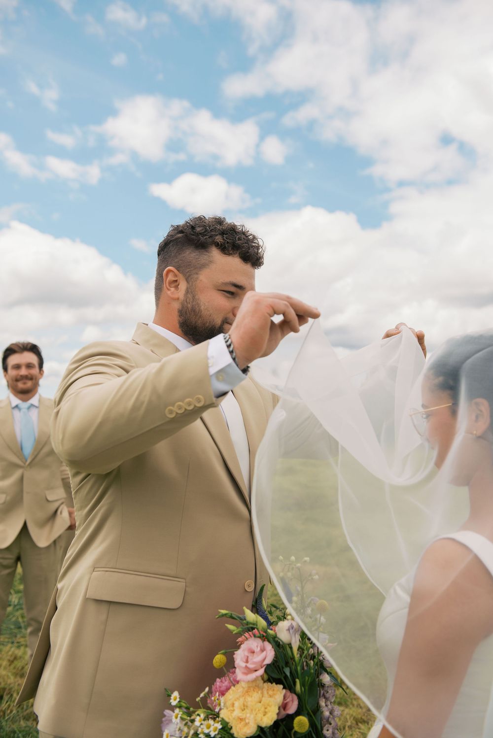 Emotional wedding first look moment captured in sunny meadow.
