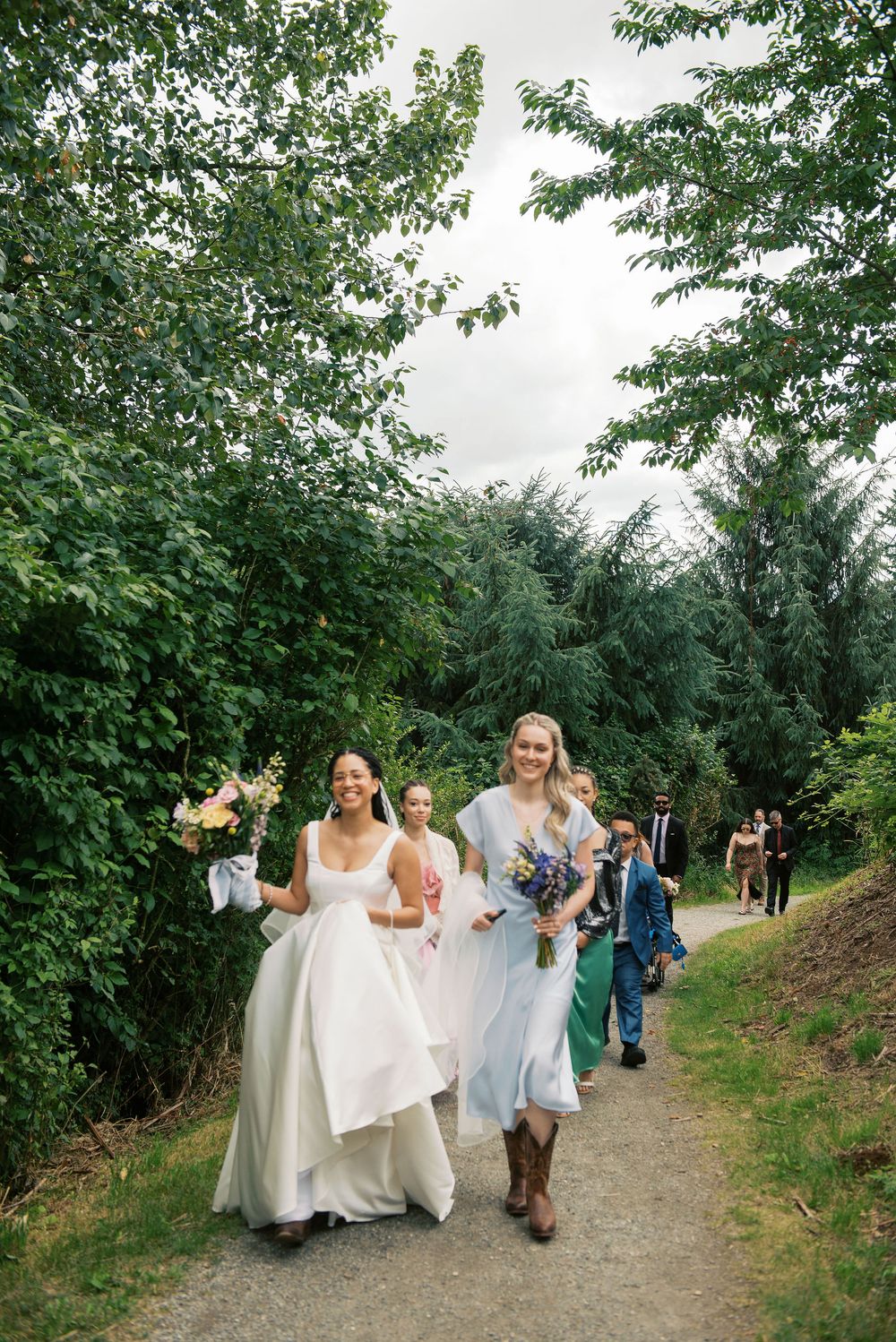 Wedding party walking along a tree-lined path during an outdoor celebration.