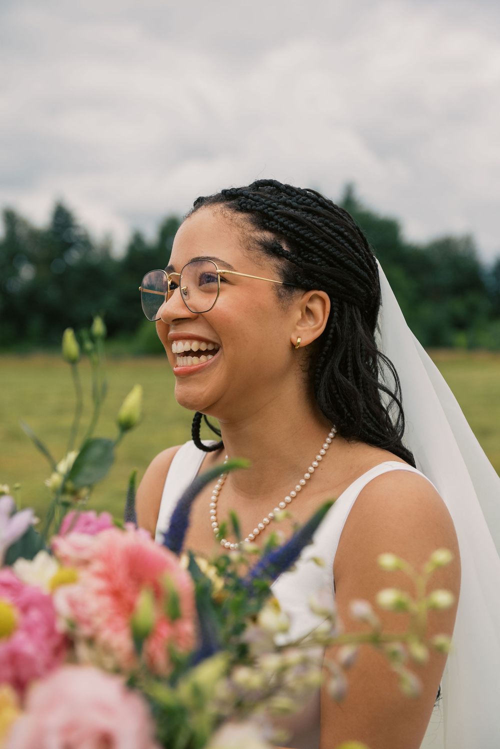 Bride with a radiant smile holds colorful floral bouquet during outdoor ceremony.