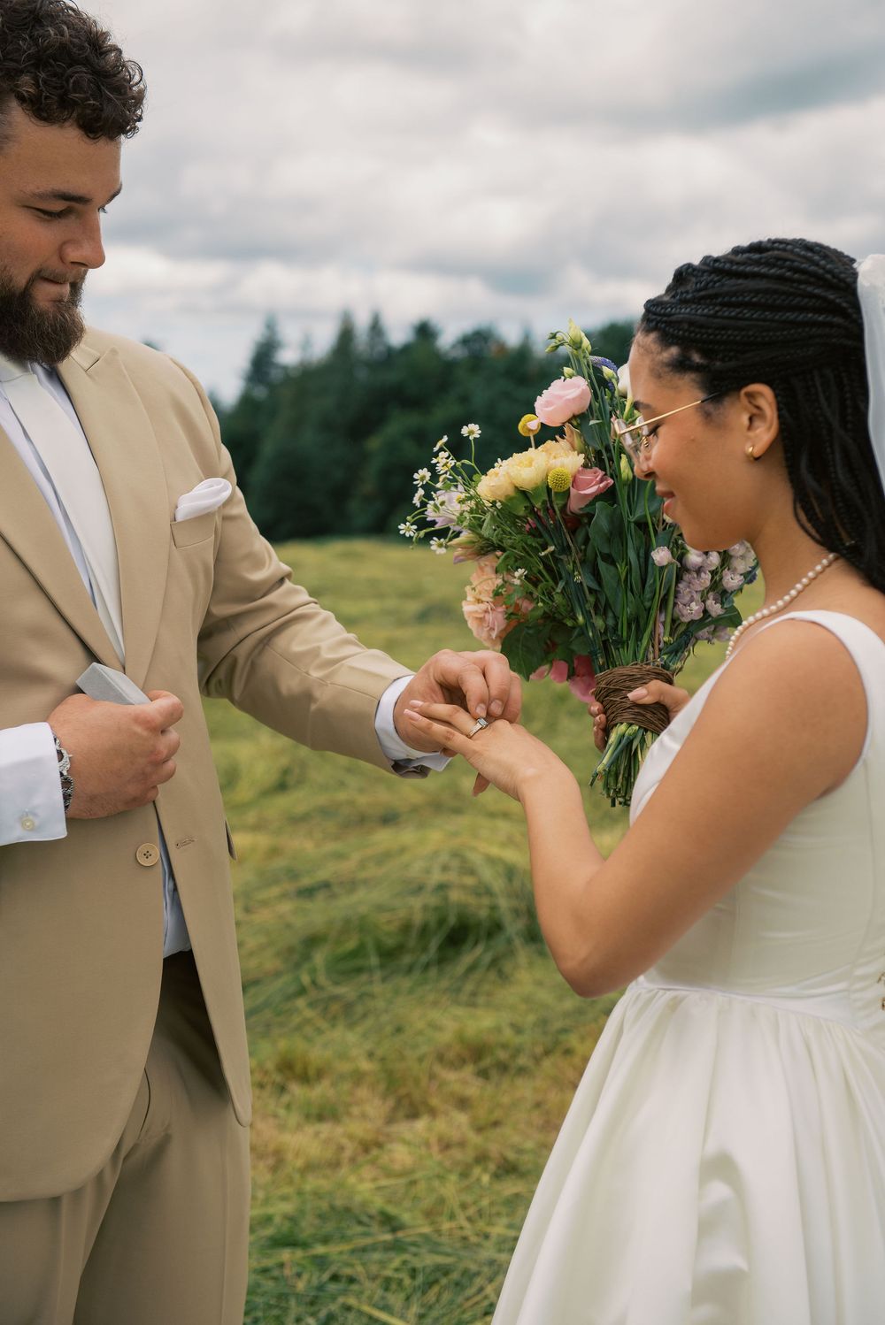 Couple exchanges rings during outdoor wedding ceremony surrounded by wildflowers.