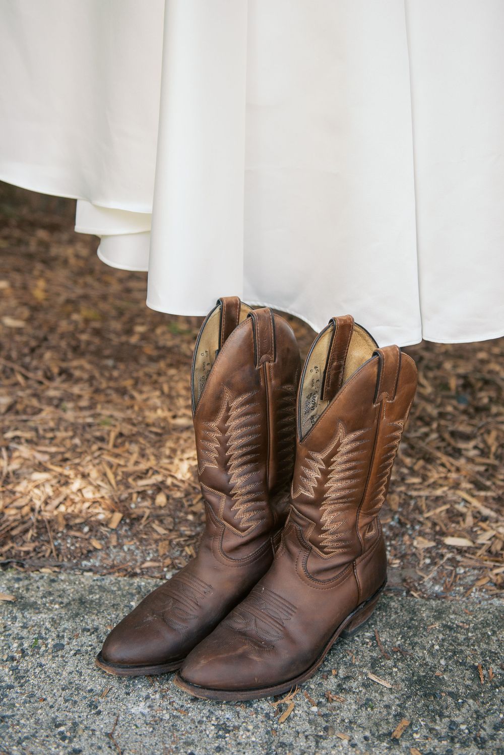 Brown leather cowboy boots beneath the hem of a white wedding dress.