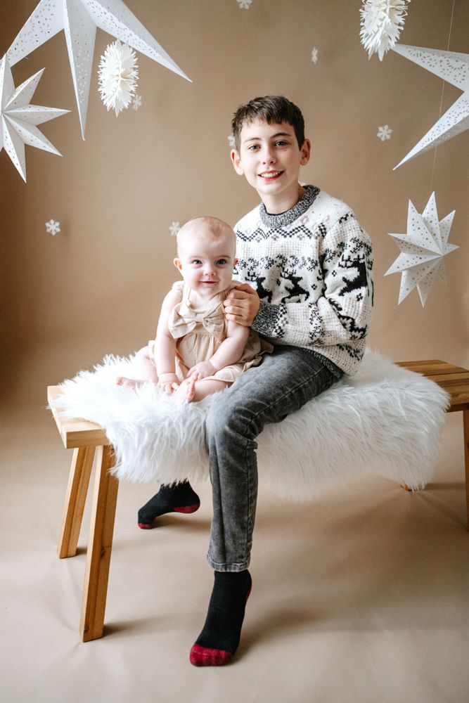 Winter photo session with white hanging star decorations and white fur bench as children pose for holiday portraits.
