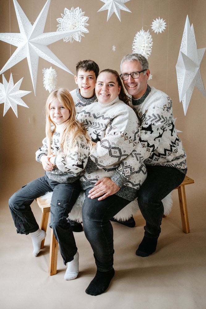 A group wearing matching nordic sweaters sits together in front of white paper star decorations for a holiday photo.