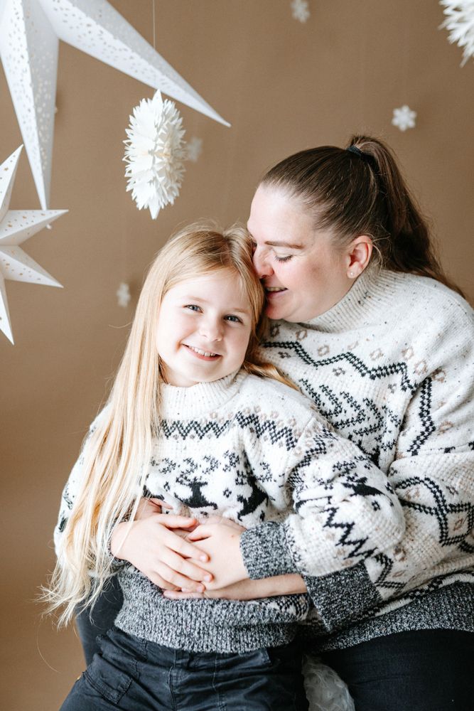 A heartwarming winter family photoshoot with matching Nordic sweaters against a beige backdrop with white paper star decorations.