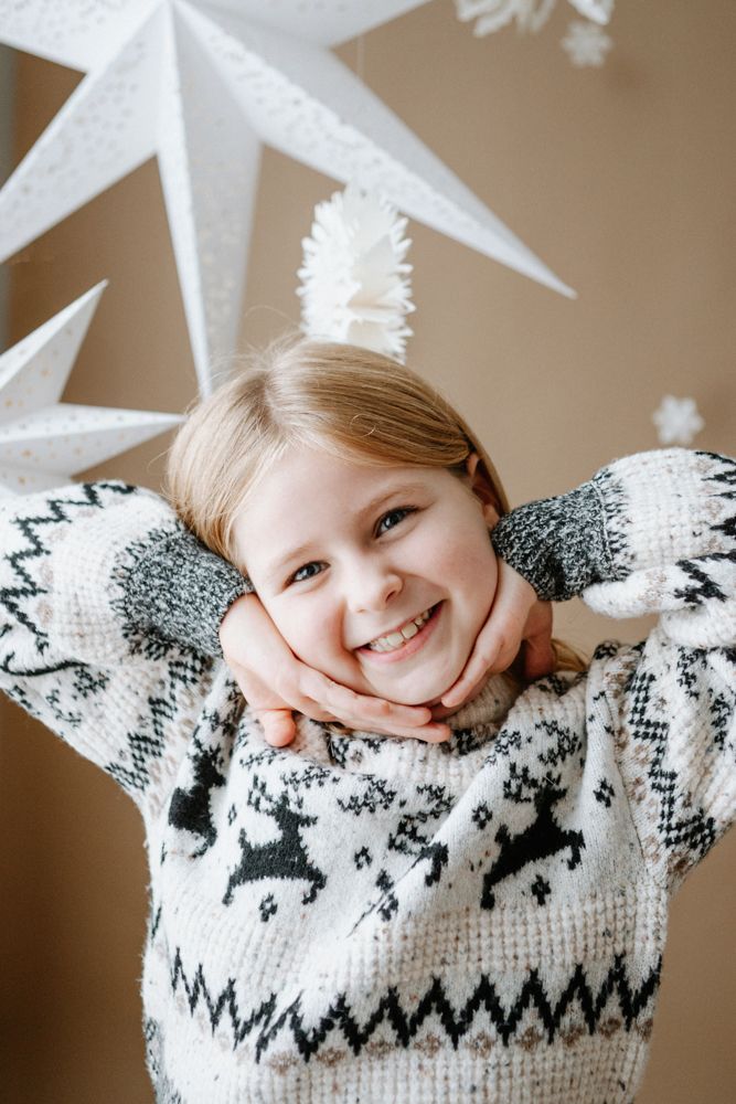 Child wearing a cozy winter sweater with Nordic pattern rests head on hands while lying down.