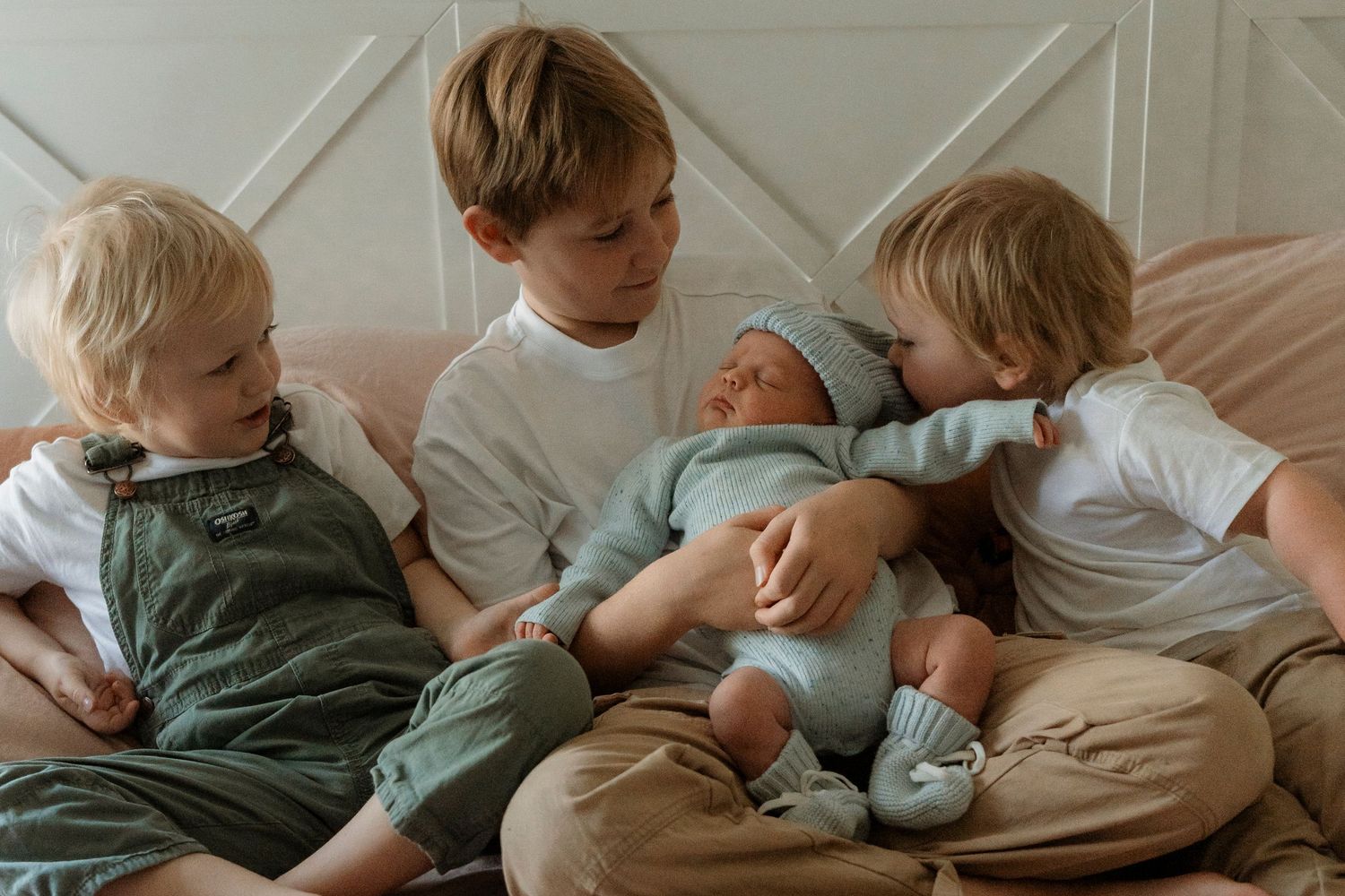Children relaxing kissing their newborn brother on the bed, casual, natural together on a comfortable couch in a cozy living room setting.