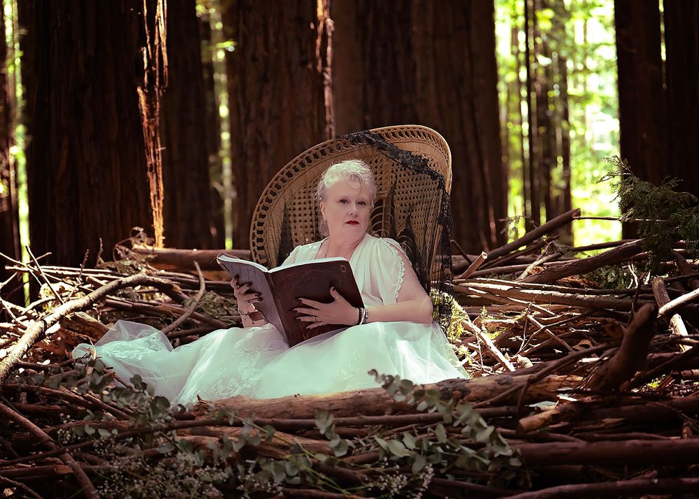 Woman dressed in white outfit sits in a peacock chair located in a handmade nest in the warburton redwoods