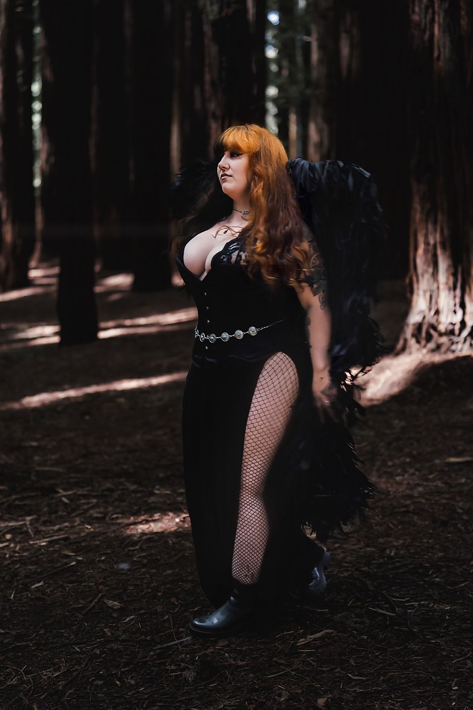 Figure with red hair in dark gothic attire poses dramatically in a shadowy forest setting.