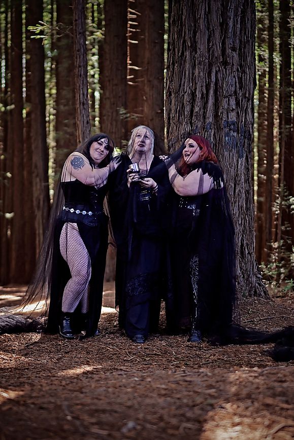 Four people in black outfits pose together in a redwood forest setting with dramatic lighting.