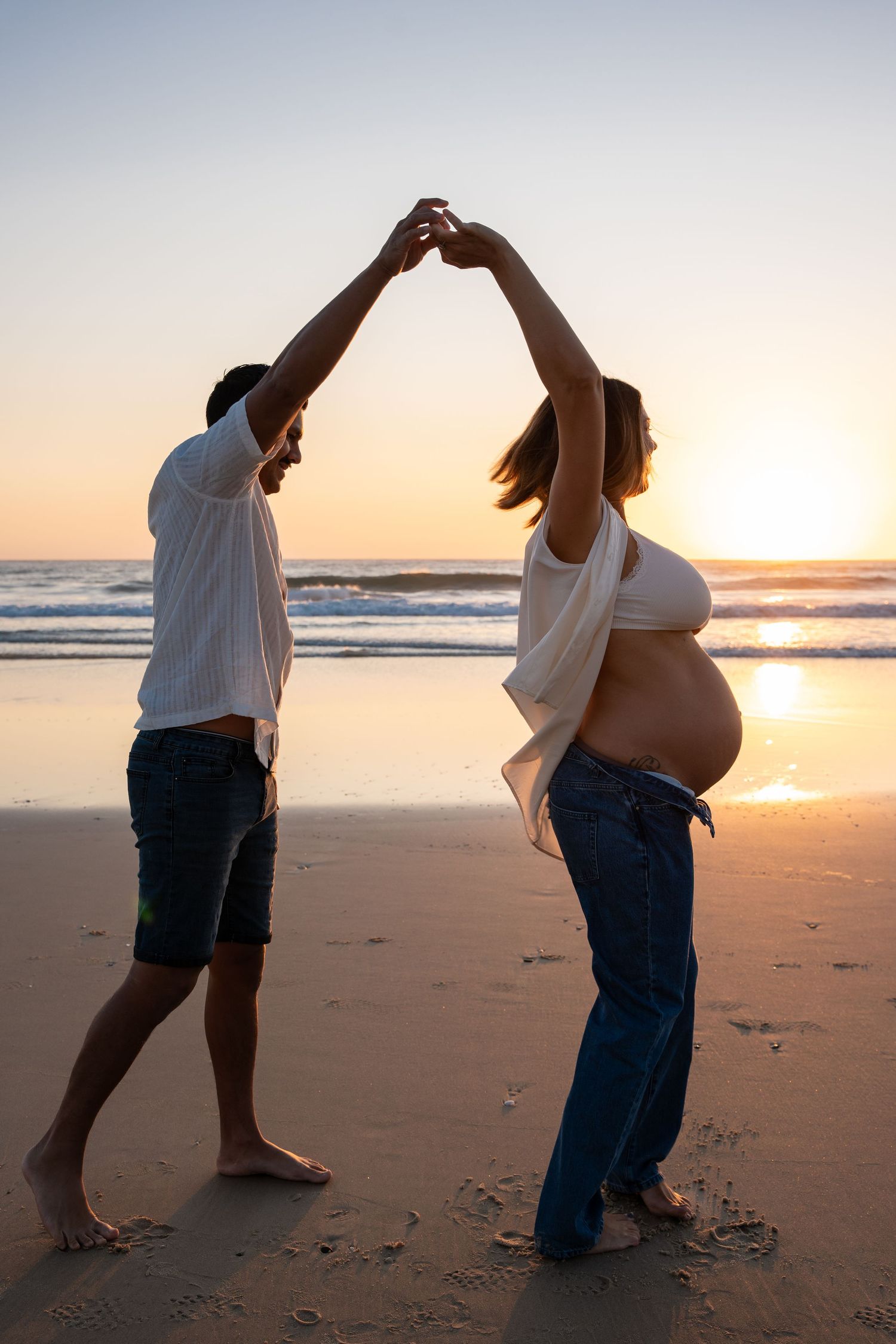 Couple dancing playfully on a sunset beach, casting silhouettes against the golden sky and ocean waves.