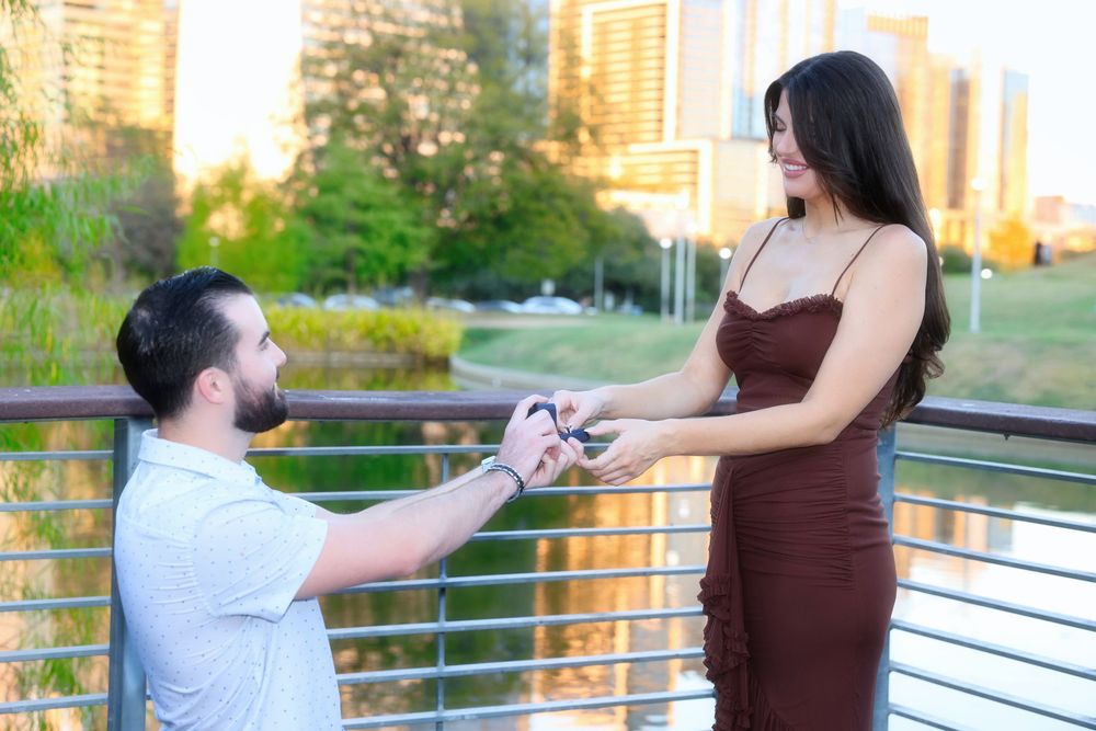 A marriage proposal taking place on a balcony overlooking a city park during golden hour.