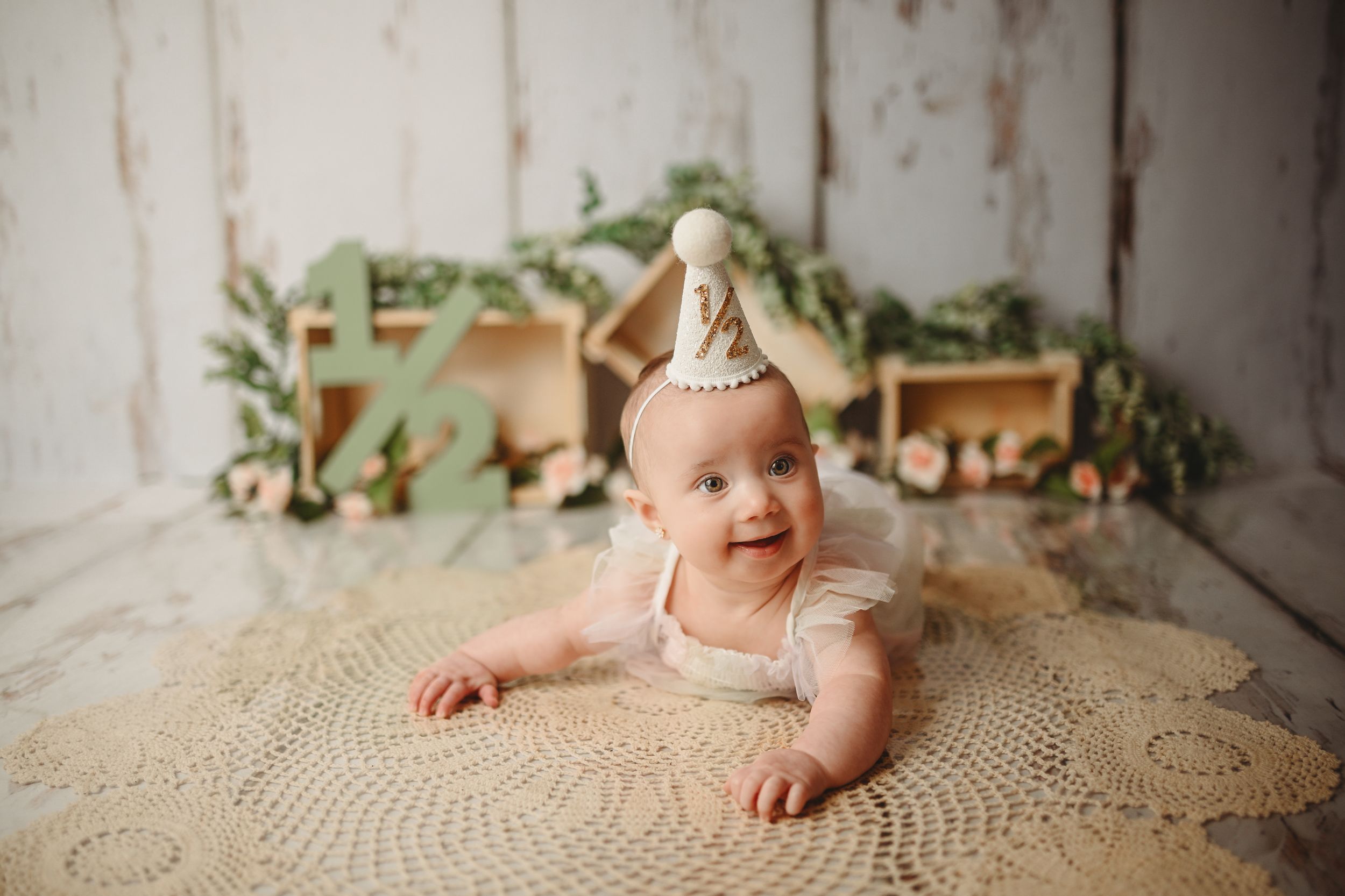 Baby smiling while lying in rattan bassinet on textured neutral backdrop.