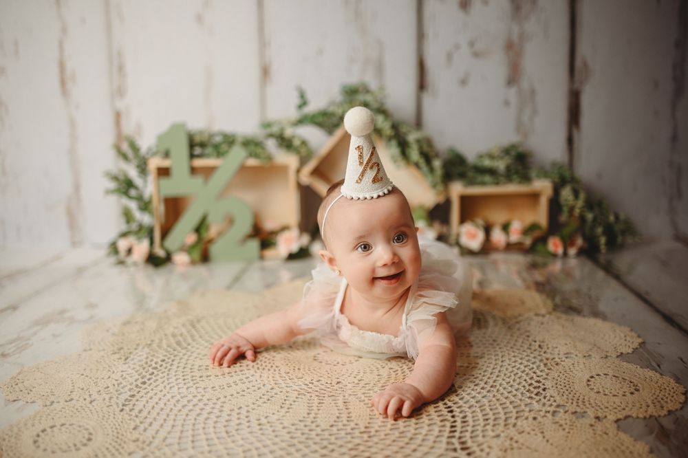 Baby smiling while lying in rattan bassinet on textured neutral backdrop.