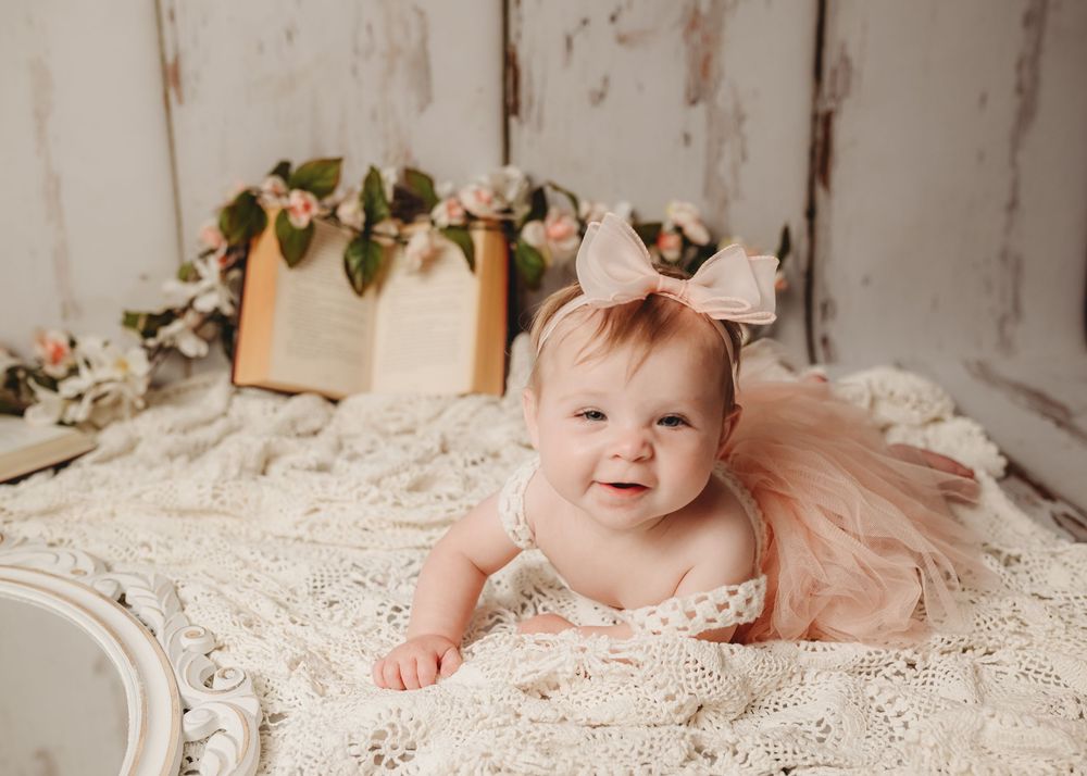 Baby in pink tulle dress posing on lace blanket for portrait session.
