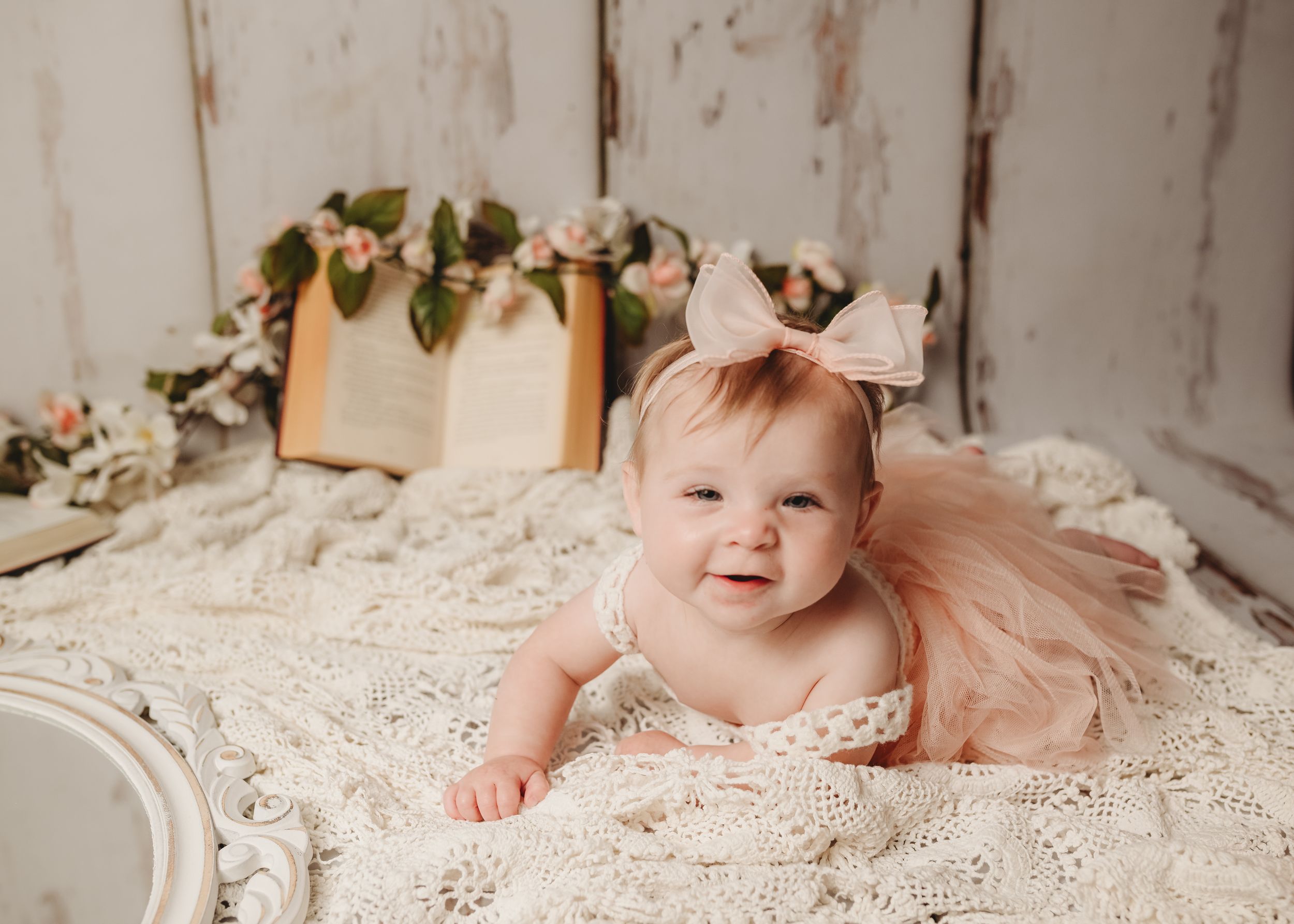Baby in pink tulle dress posing on lace blanket for portrait session.