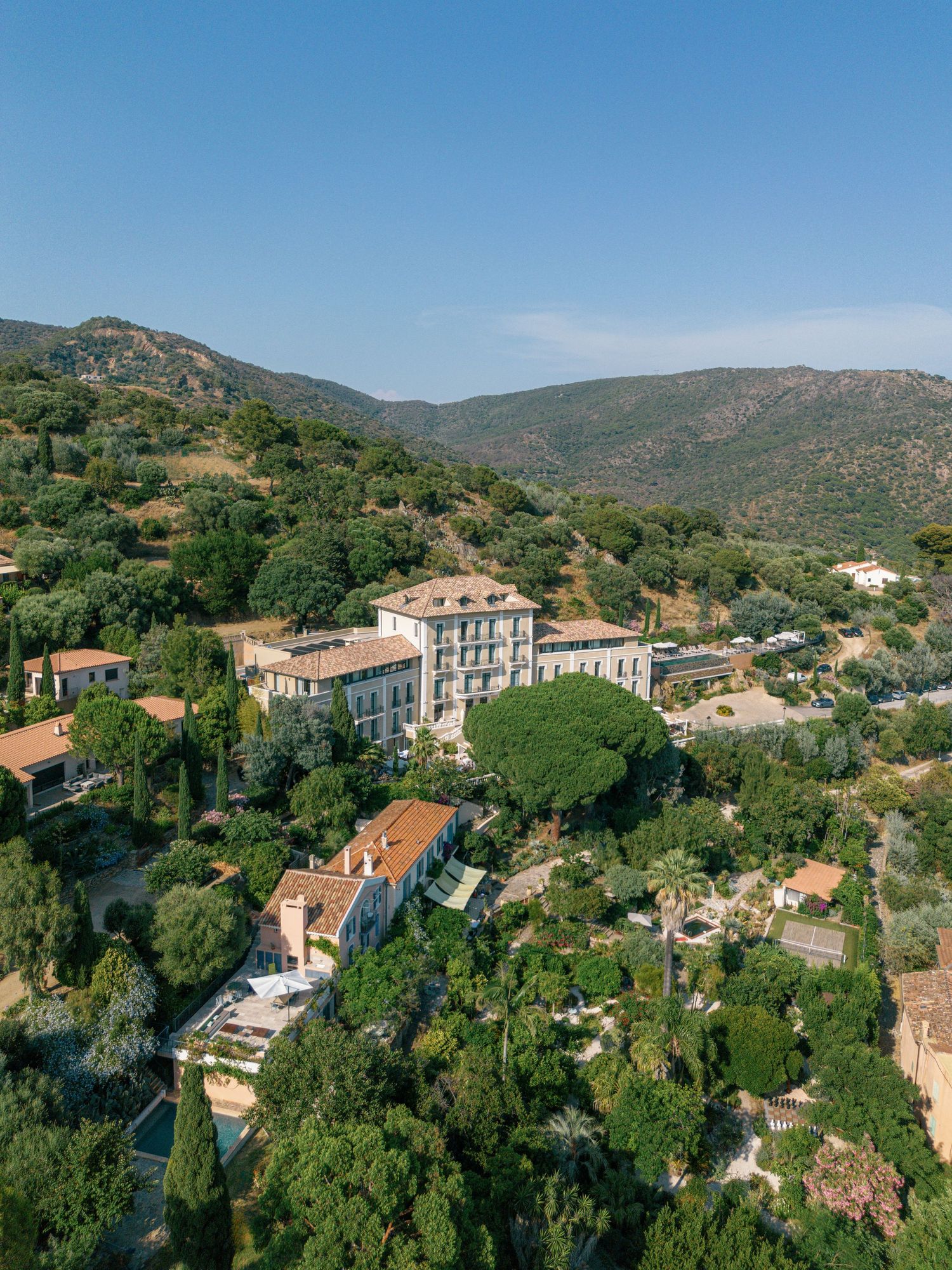 Panoramic view of small Mediterranean village with Eden Rose Grand Hôtel, Bormes-les-Mimosas nestled in green hills under blue sky.