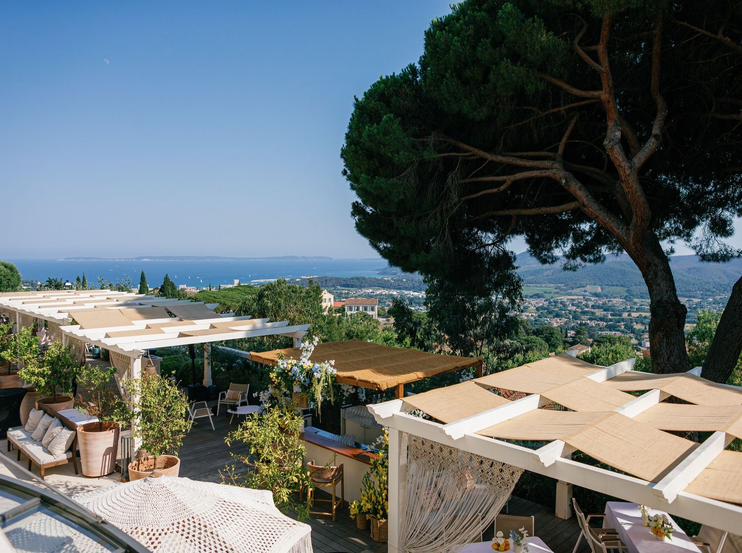 A Mediterranean coastal property features sweeping views of the sea with lush trees and elegant architecture.