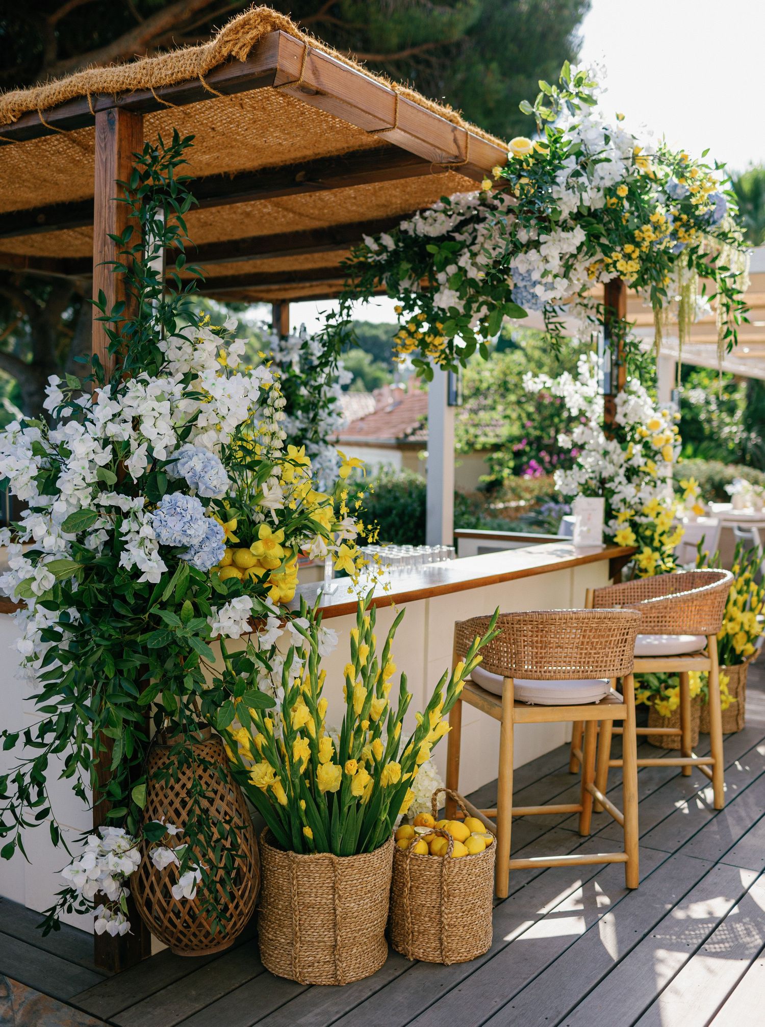 Wooden deck patio decorated with woven baskets, rattan furniture, and climbing white and yellow flowering vines on a pergola.
