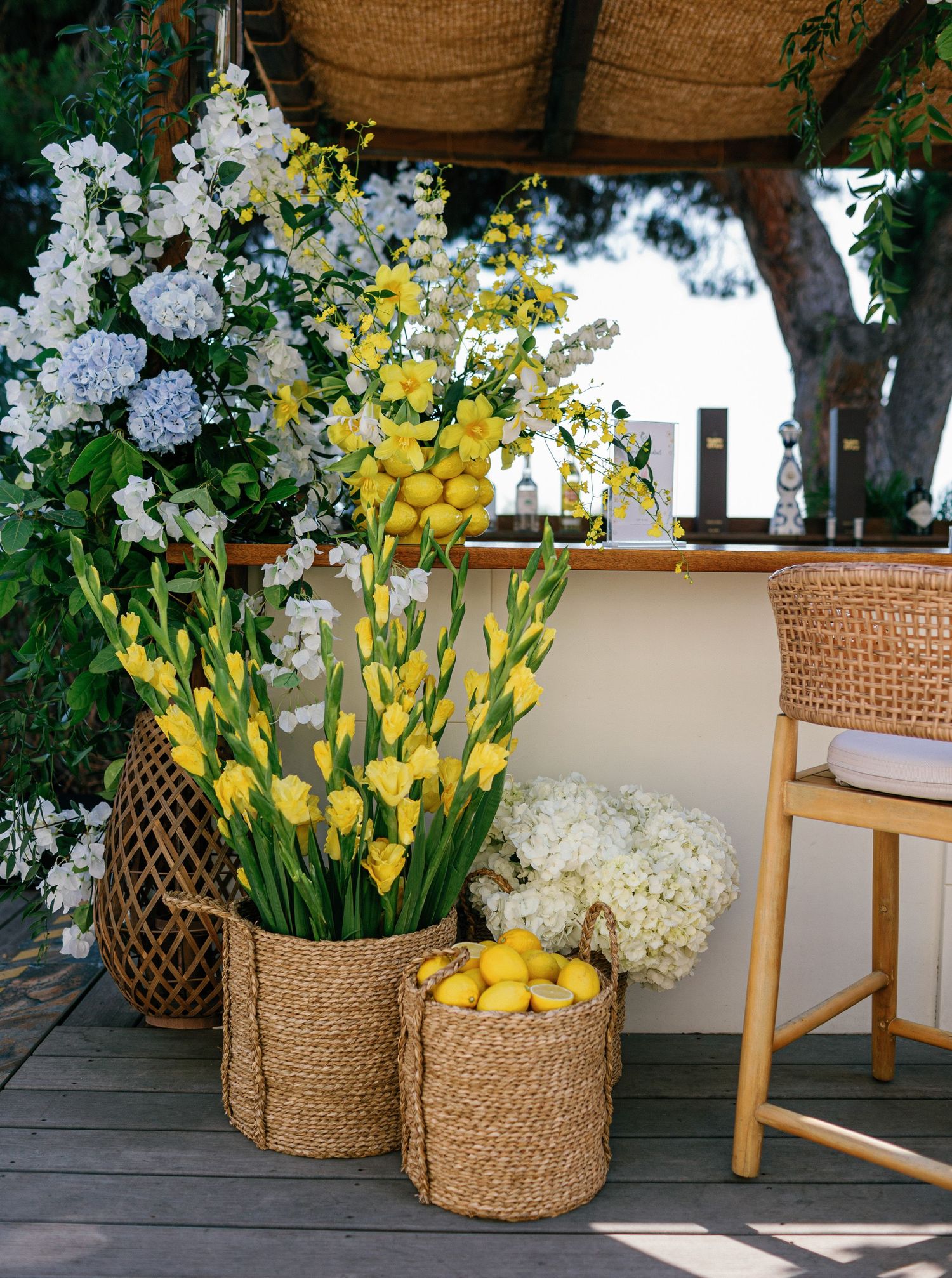 Natural woven baskets filled with fresh lemons and white and yellow flowers arranged on outdoor wooden deck.