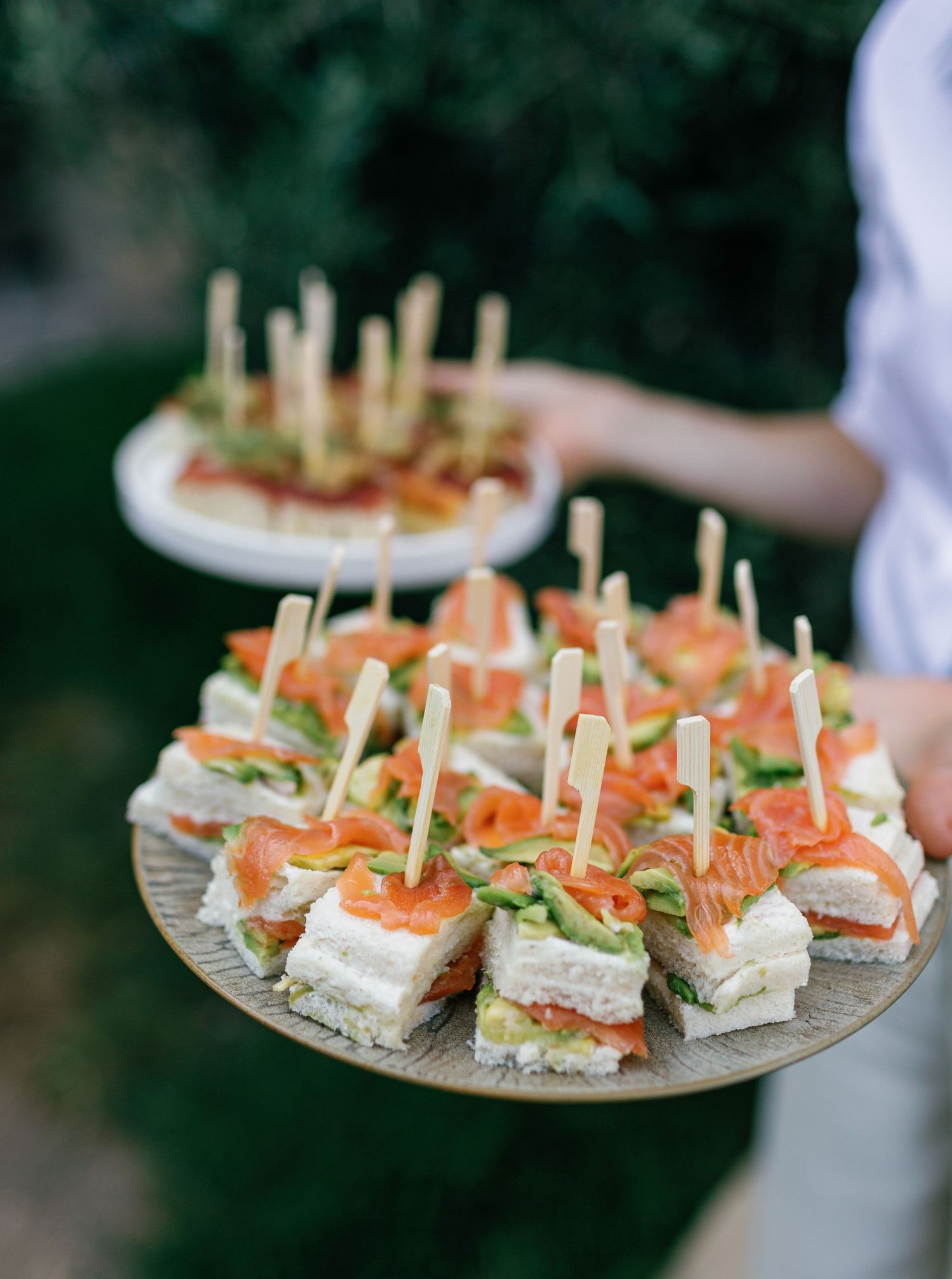 Plate of elegant finger sandwiches with smoked salmon, cream cheese and cucumber garnished with fresh herbs.