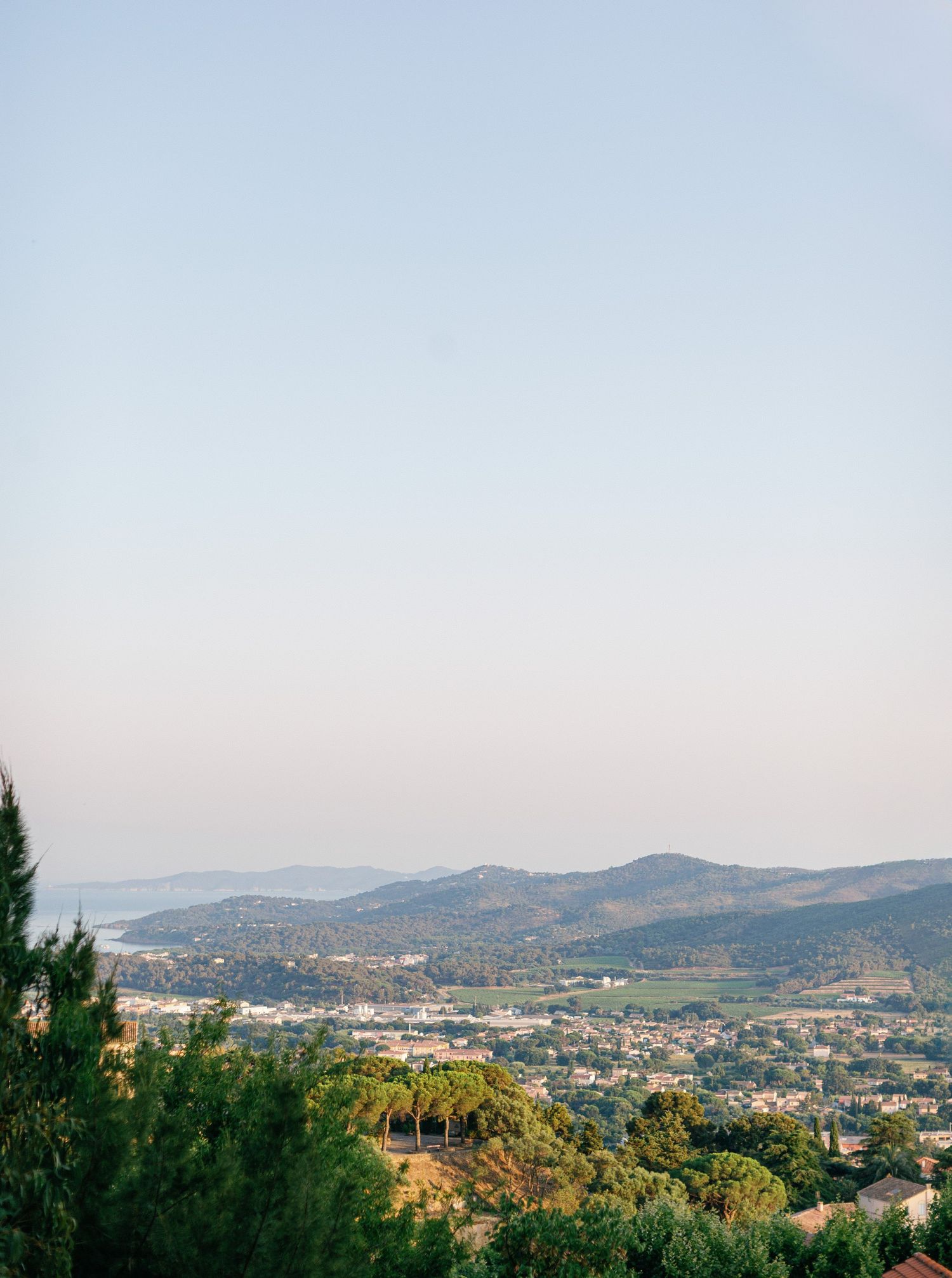 Panoramic mountain vista showing expansive hills, town buildings, and green vegetation under a clear blue sky.